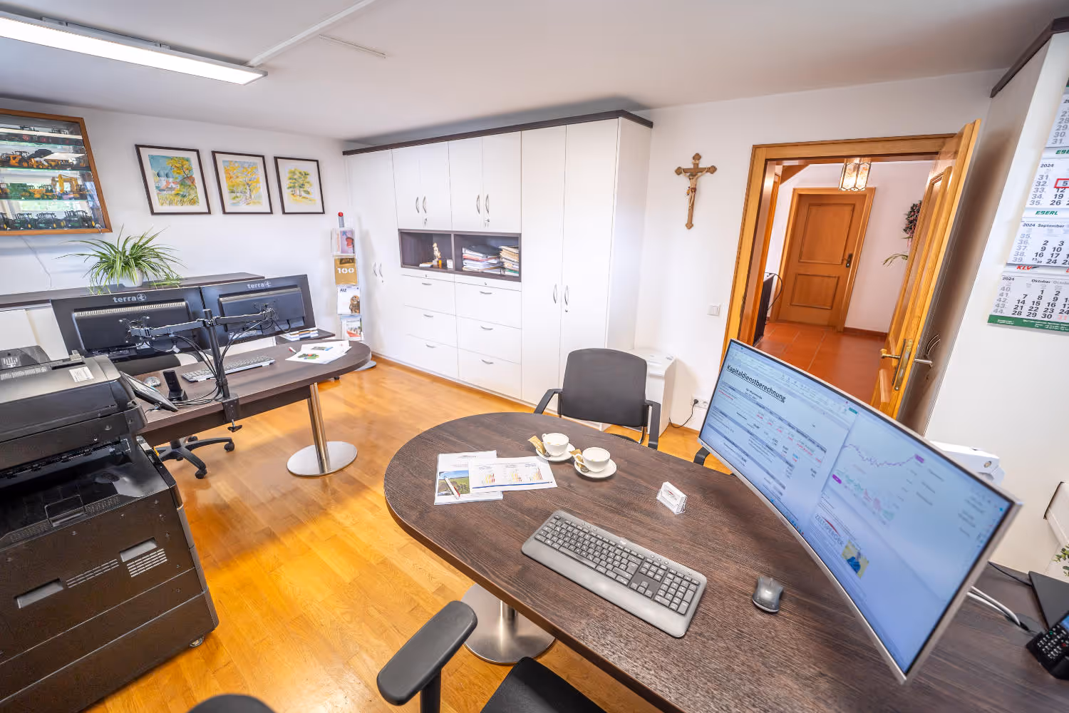 Helles Büro von Zeltsperger Immobilien und Wirtschaftsberatung mit Auszeichnungen an der Wand, braunem Bürotisch und Desktops und Tür.