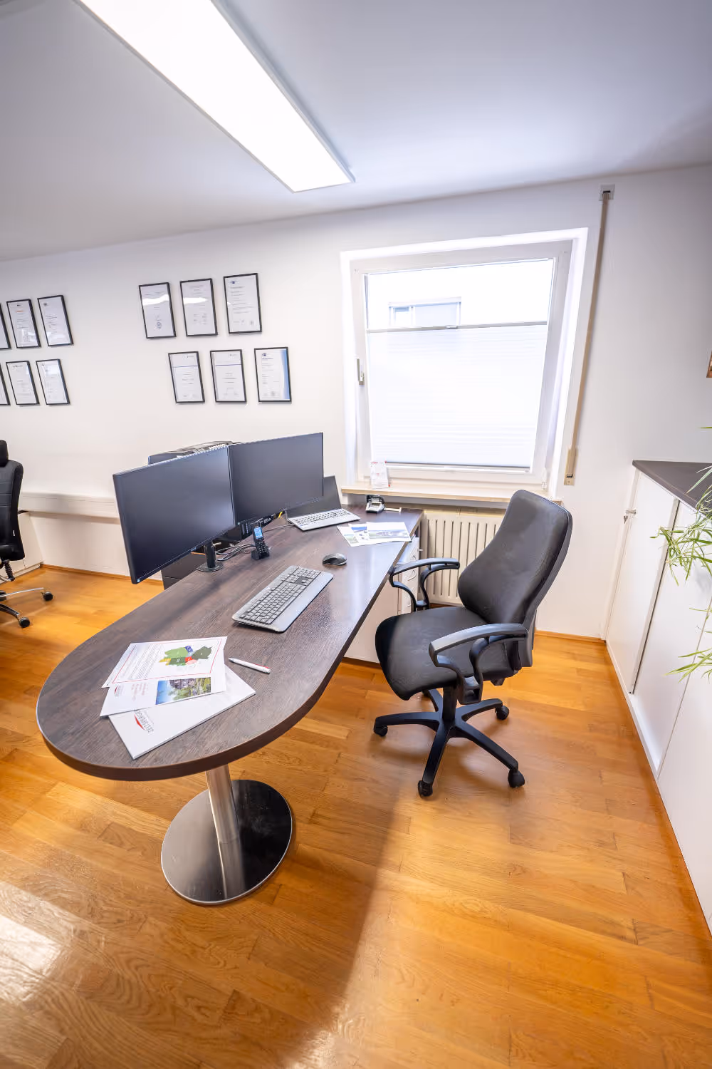 Helles Büro von Zeltsperger Immobilien und Wirtschaftsberatung mit Auszeichnungen an der Wand, braunem Bürotisch und Desktops.