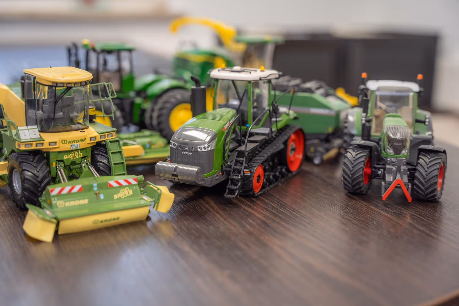 Detailaufnahme mehrerer Modelltraktoren und Landmaschinen auf einem Holztisch, Symbol für regionale Verbundenheit und landwirtschaftliche Expertise.