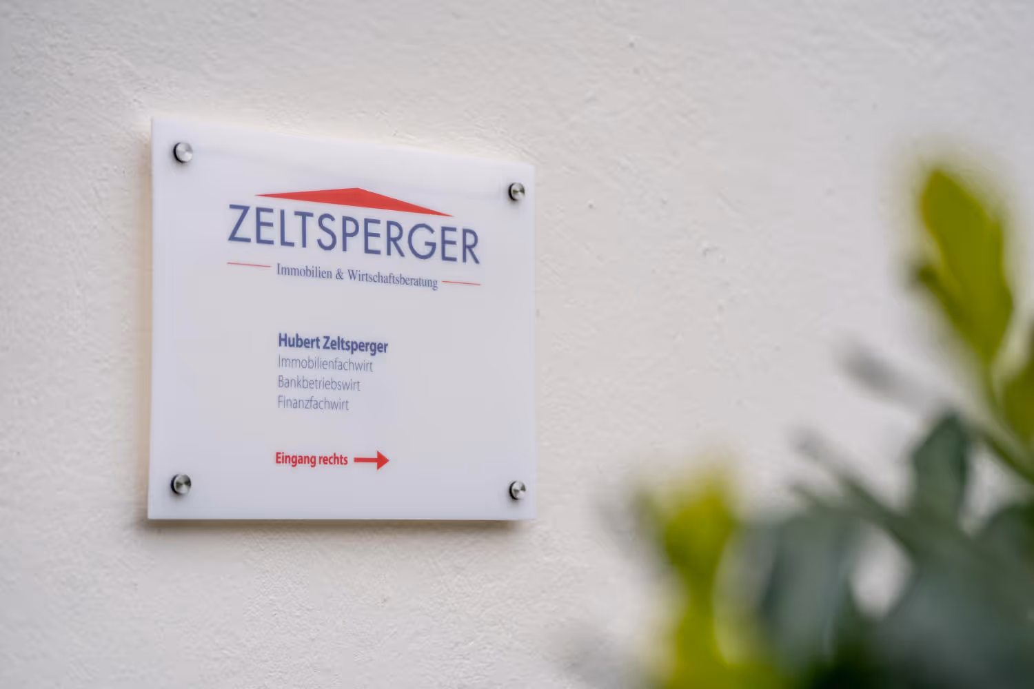 Zeltsperger Immobilien und Wirtschaftsberatung Schild, das an der Wand hängt und zum Eingang weist. Wegweiser.