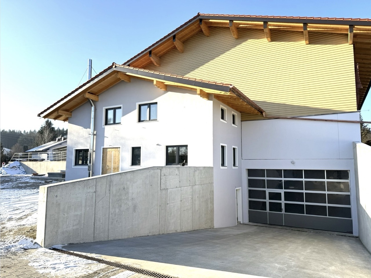 Modernes Einfamilienhaus mit weißer Fassade, Satteldach, großer Doppelgarage, Holzverkleidung, überdachter Terrasse und sonniger Hanglage – energieeffizientes Eigenheim mit Bergblick und viel Platz für Familien.