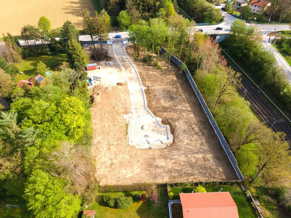 Luftaufnahme eines eingezäunten Baugrundstücks mit Fundamentvorbereitung, umliegender Grünanlage, Nachbarbebauung und ruhiger Siedlungslage – sonniges, erschlossenes Grundstück für Neubau-Einfamilienhaus oder Doppelhaus.