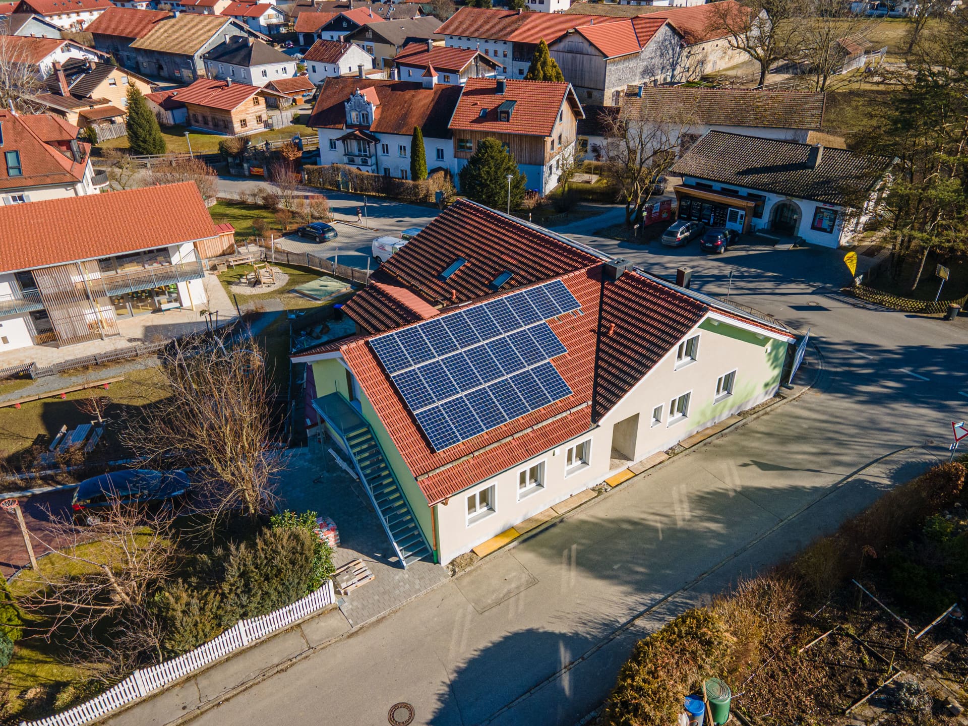Freistehendes Einfamilienhaus mit roter Dachziegelung, Photovoltaikanlage, weißer Fassade und großem Grundstück – energieeffizienter Neubau in ruhiger Siedlungslage mit Bergblick aus der Luft.