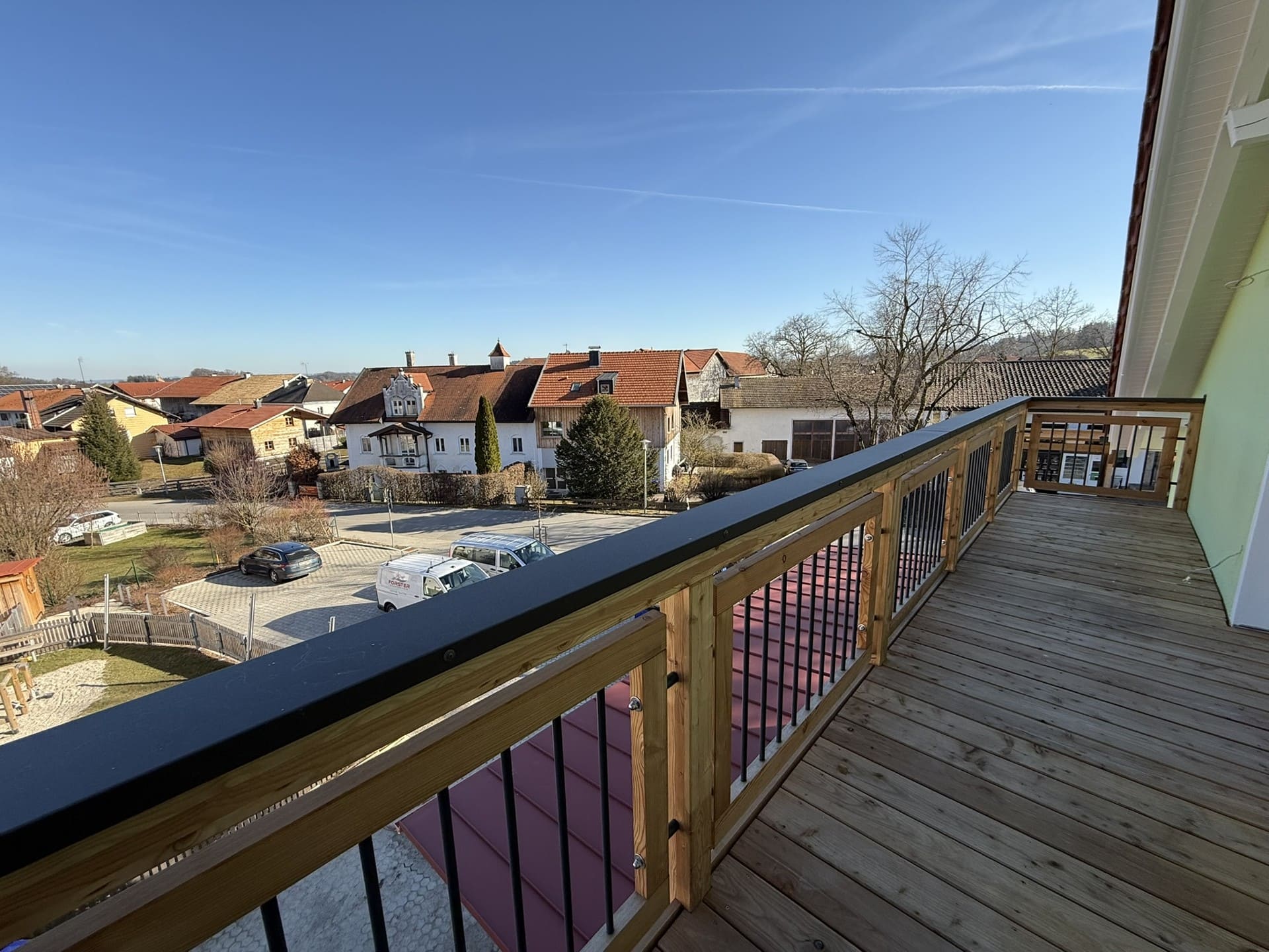 Balkon mit Holzgeländer und Aussicht – sonniger Außenbereich mit Blick auf die Dorfmitte von Tengling