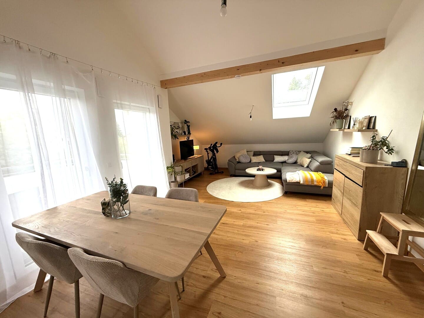 Heller Dachgeschoss-Wohnbereich mit Holzdielenboden, großem Esstisch für 6 Personen, gemütlicher Sitzecke, Dachschrägen und bodentiefen Fenstern mit viel Tageslicht – offenes, modernes Wohnen im Einfamilienhaus.