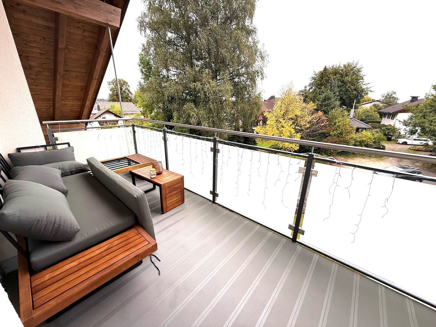 Überdachter Balkon mit Sitzmöbeln und Glasgeländer – sonniger Giebelbalkon der Dachgeschosswohnung in Obing