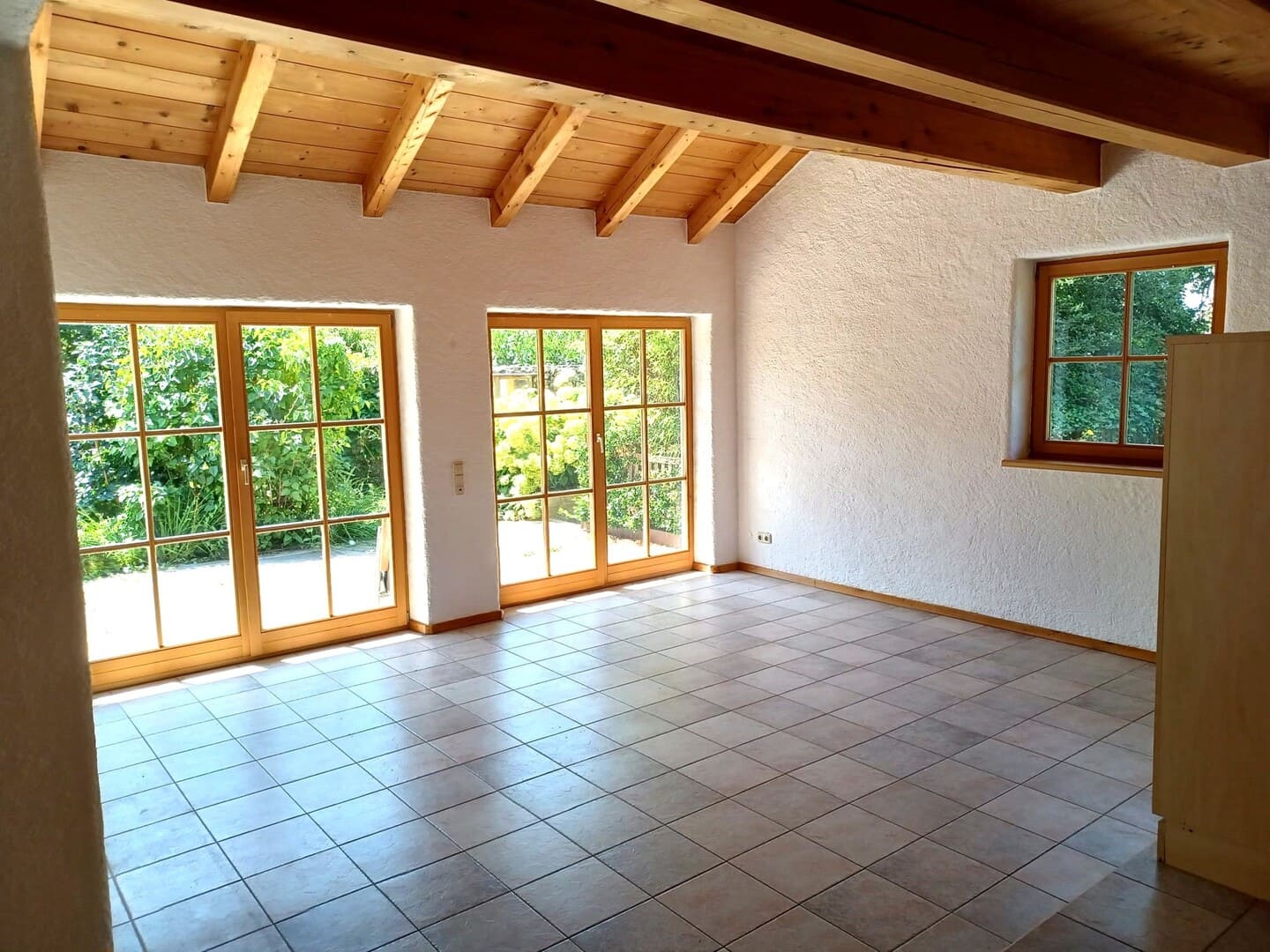 Lichtdurchflutetes Wohnzimmer mit großen Fenstern und Terrassenzugang – modernes Wohnen im Grünen.