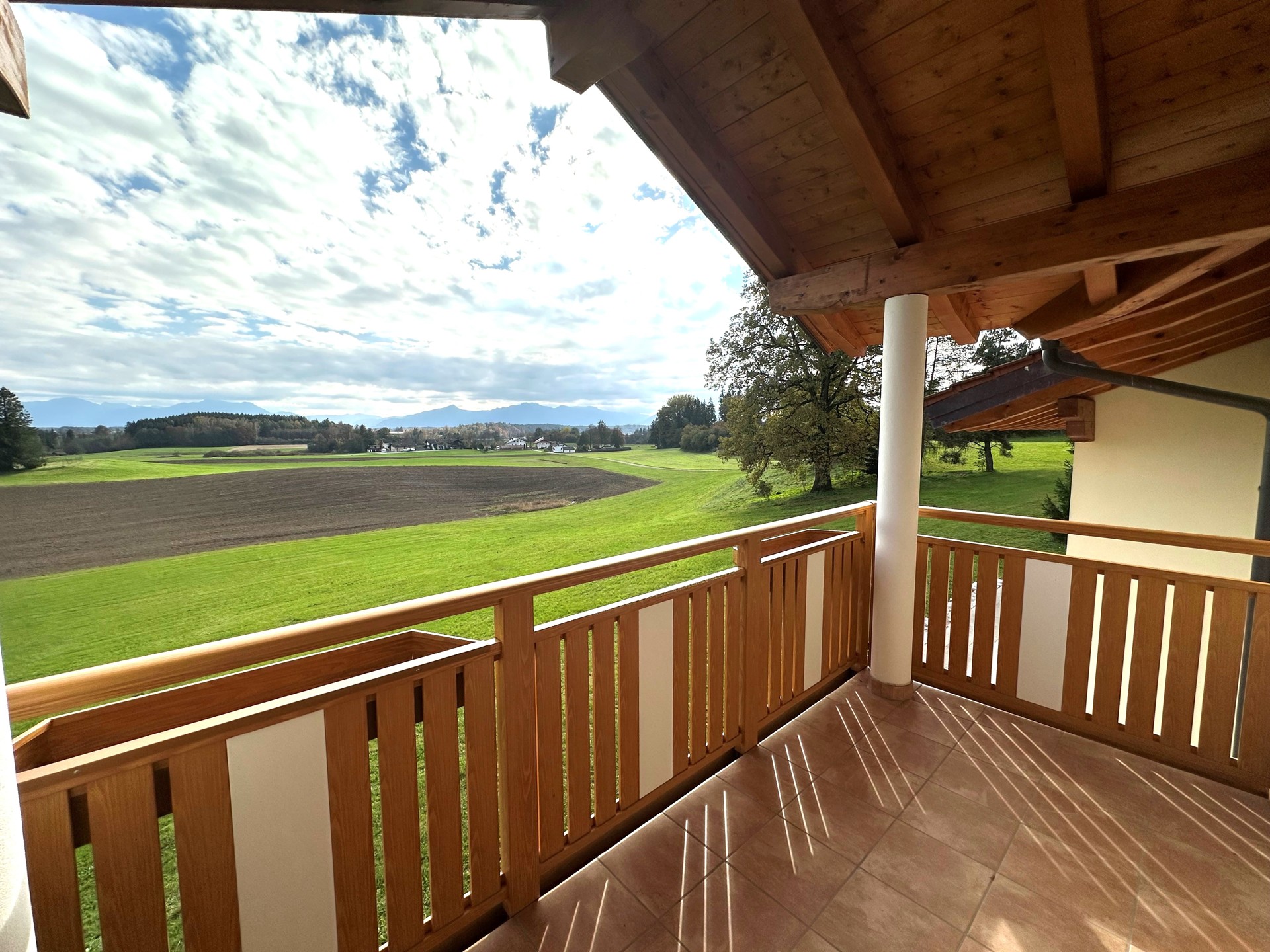 Balkon aus Holz mit weiter Aussicht über Felder und Hügel.