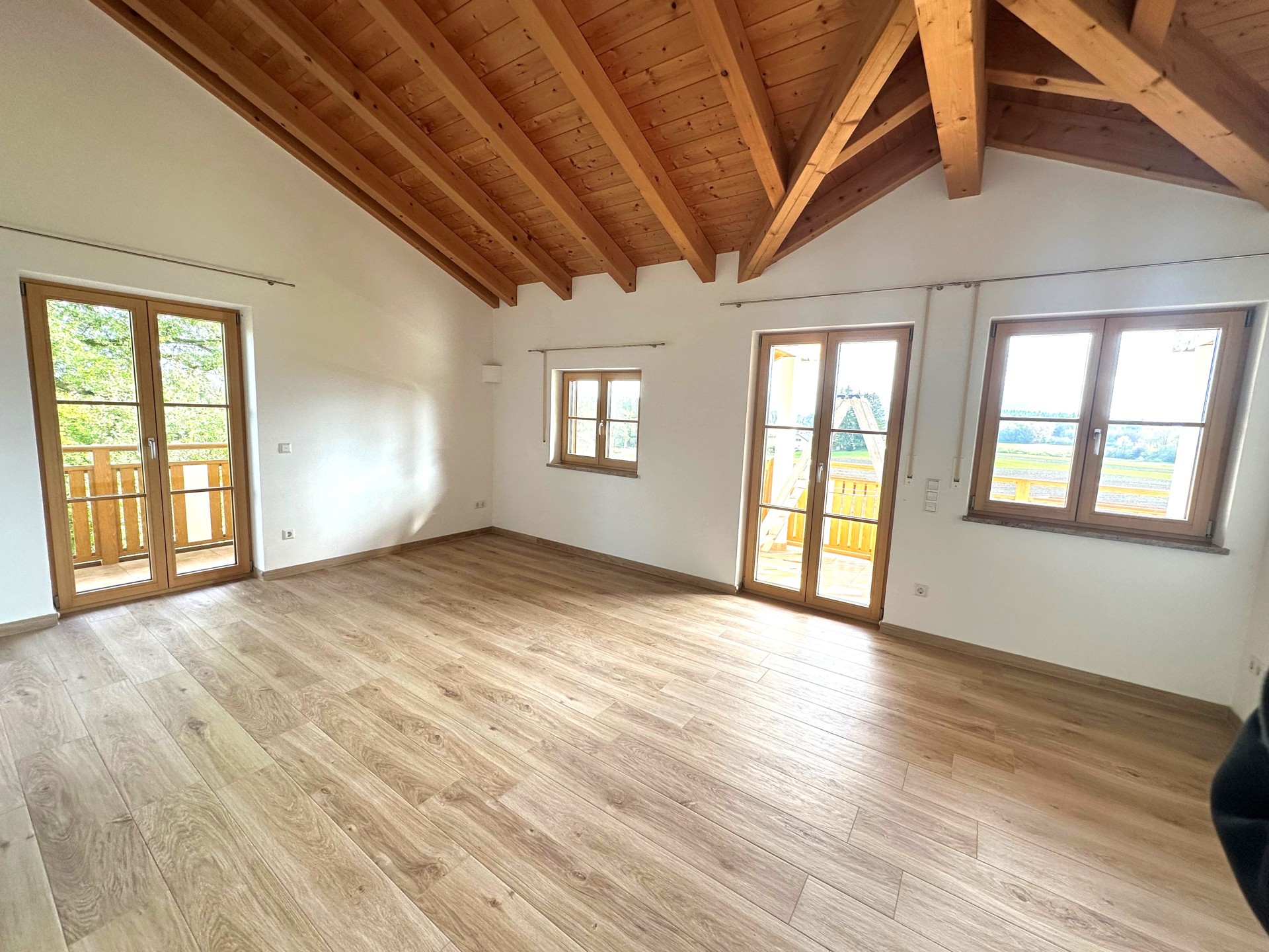 Großer Raum mit Dachschrägen, Holzbalken und mehreren Fenstern.