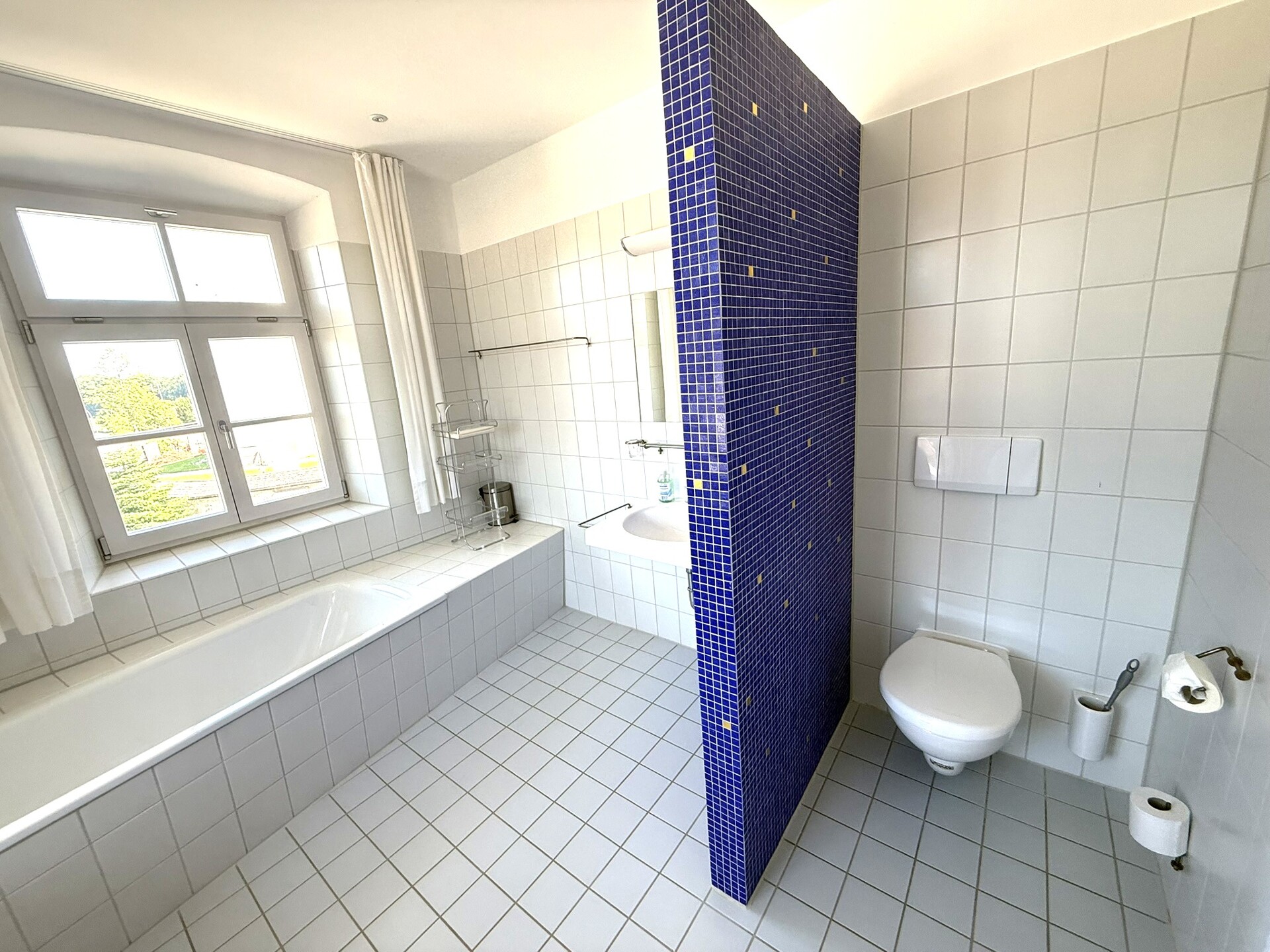 Badezimmer mit Badewanne, Dusche und blau gefliester Trennwand.