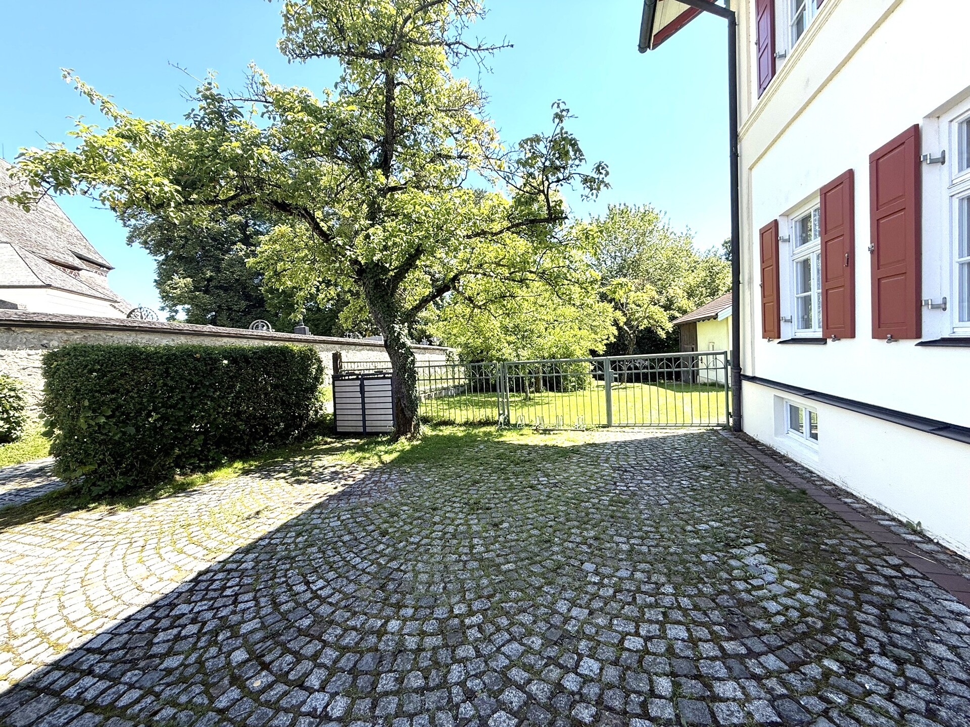 Gepflasterter Hofbereich mit Garten und Hausfassade im Hintergrund.