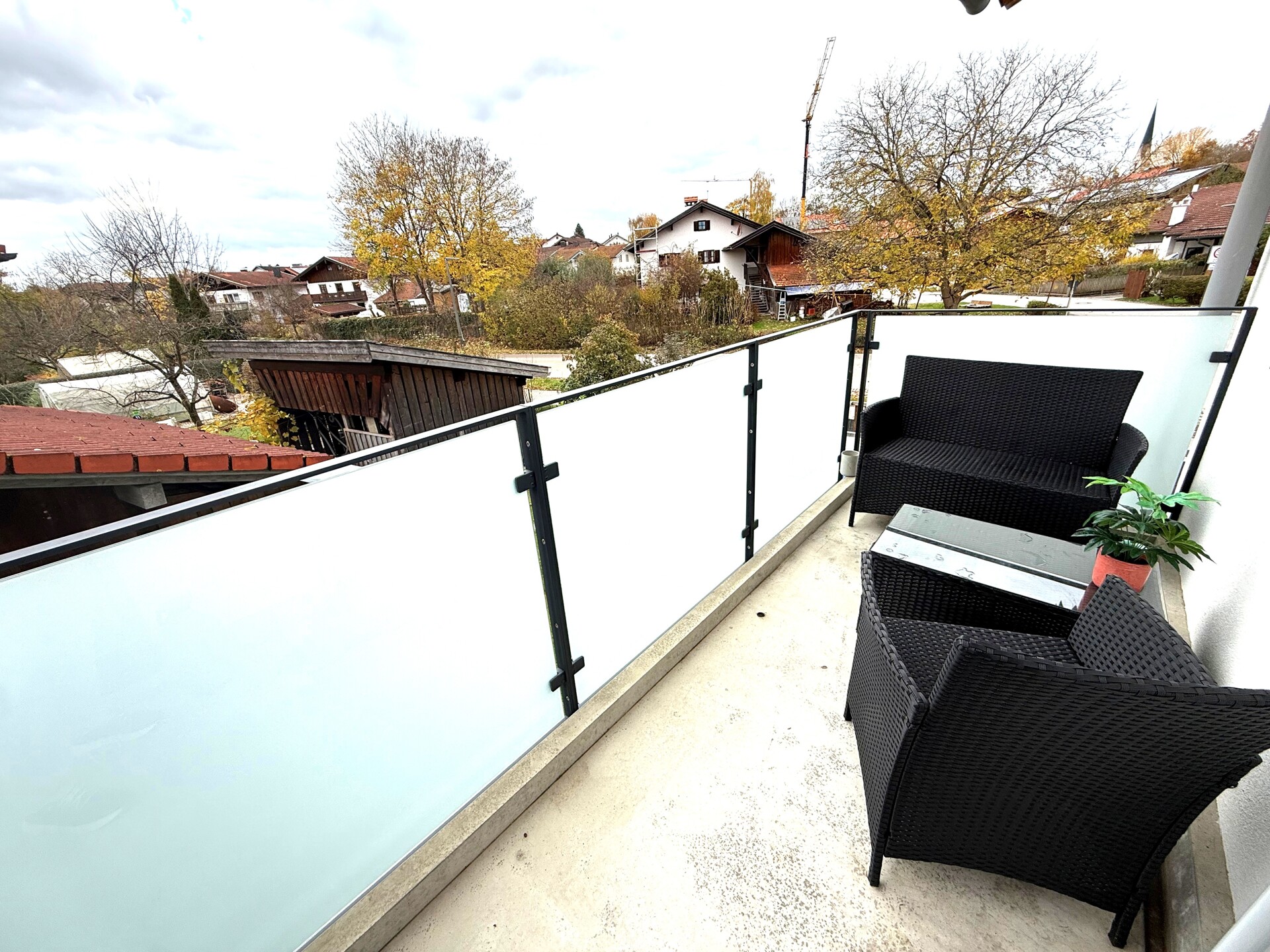 Balkon mit Glasbrüstung und Sitzmöbeln, Blick ins Wohngebiet.
