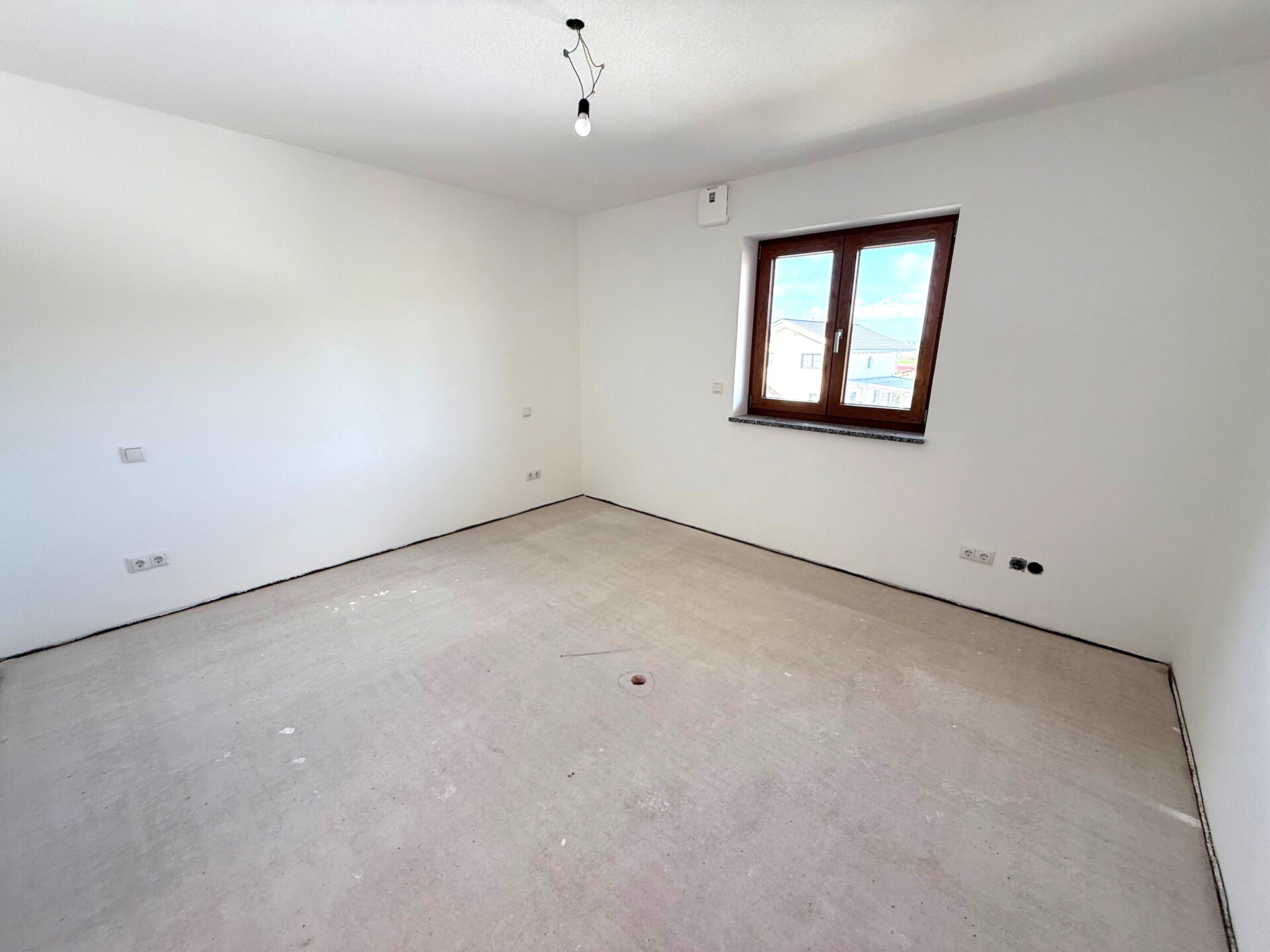 Helles leeres Zimmer mit zwei Fenstern und hellem Boden.