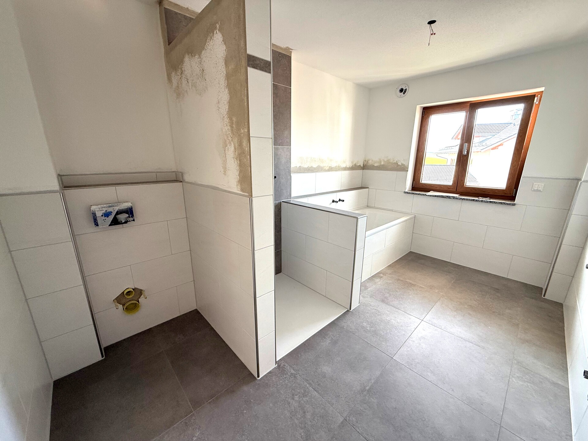 Unfertiger Küchenraum mit sichtbaren Anschlüssen und grauem Boden.