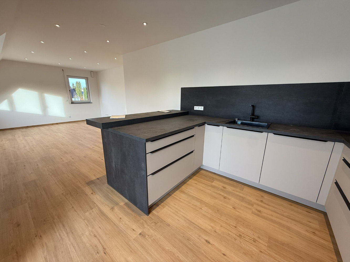 Moderner Essbereich mit Holztisch und blauen Stühlen, offener Küche mit Tresen und großen Fenstern zum Garten.