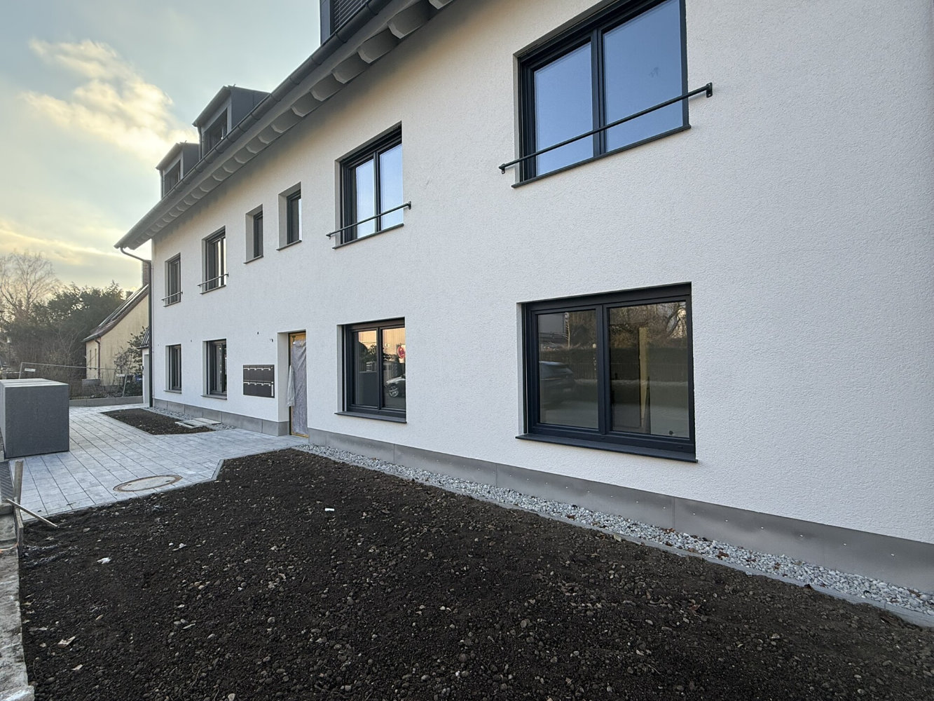 Moderner Essbereich mit Holztisch und blauen Stühlen, offener Küche mit Tresen und großen Fenstern zum Garten.