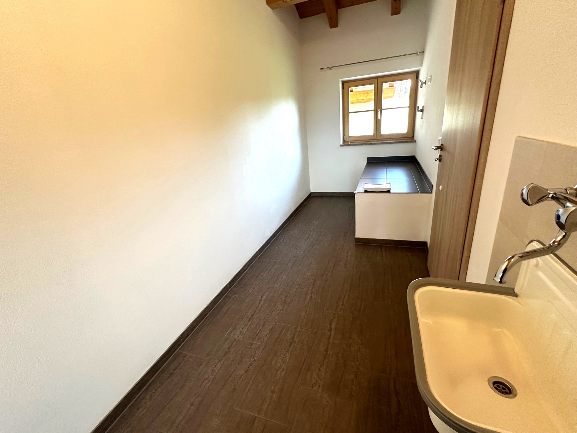 Kleiner, schmaler Raum mit Fenster und offenem Zugang zu einem Bad.