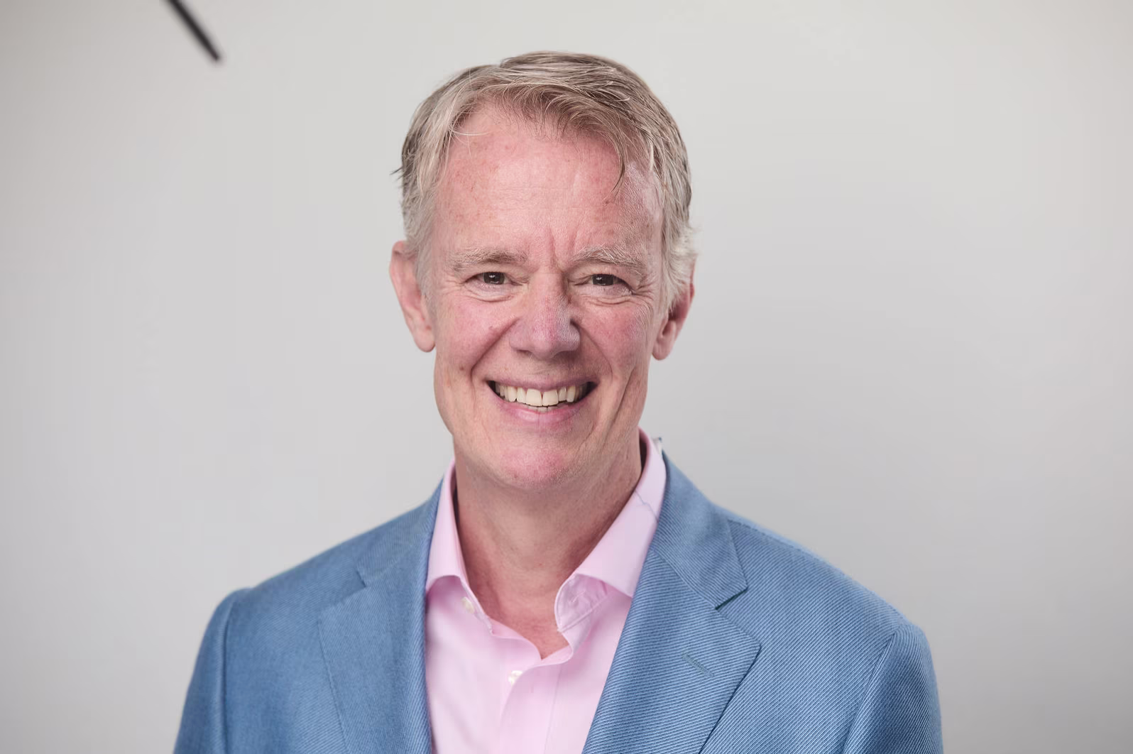 Portrait of an Michael Abbott Executive Director of GBM Securities smiling, wearing a light blue blazer and pink shirt against a light background