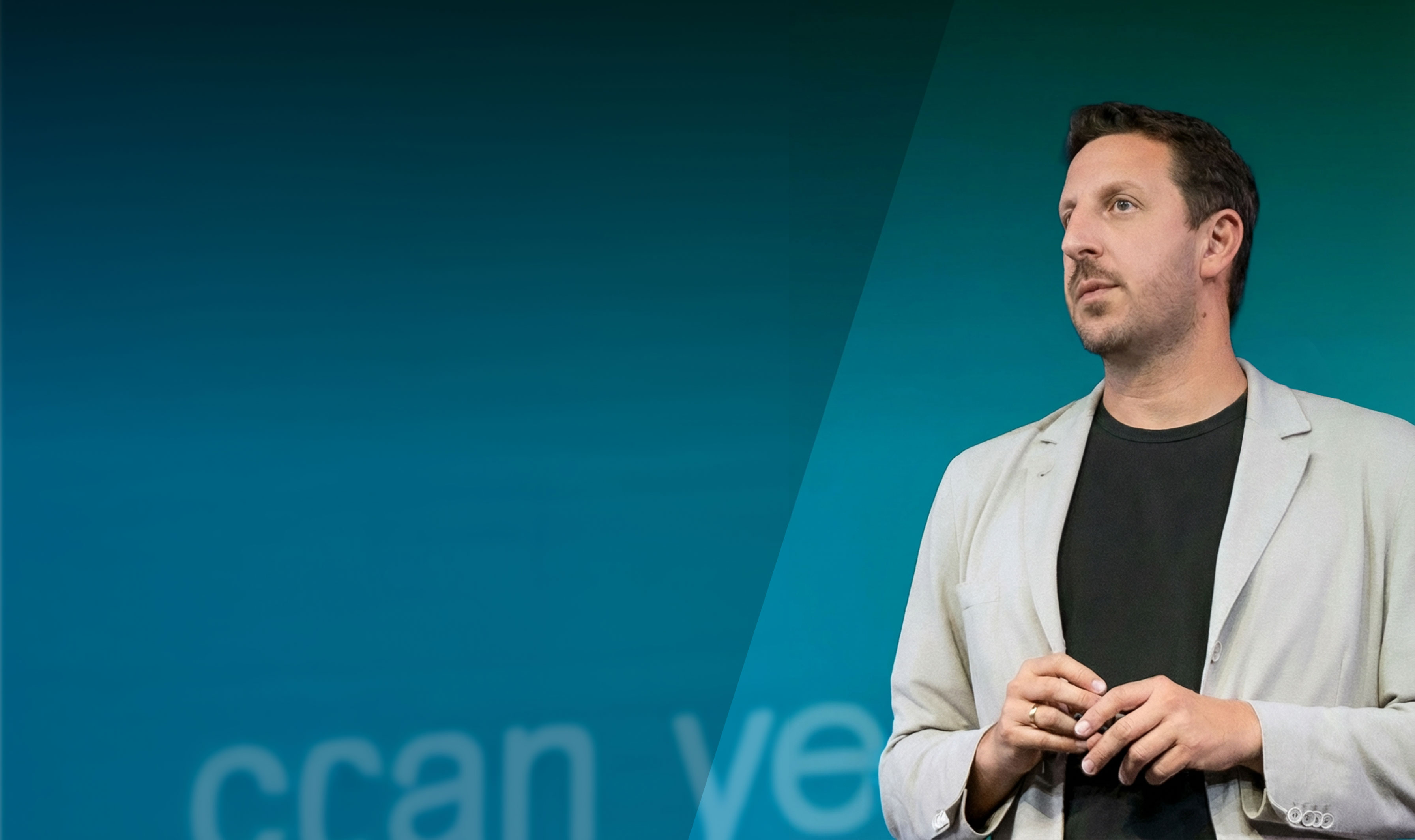 Man in beige blazer and black shirt speaking with a headset microphone against a blue gradient background.