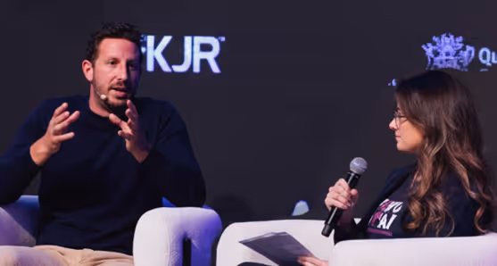 Zack Kass and a woman sit on modern chairs on a stage, engaged in a discussion during the AI Summit Brisbane 2023