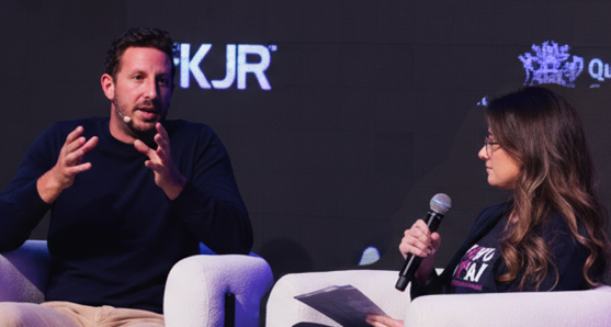 Zack Kass and a woman sit on modern chairs on a stage, engaged in a discussion during the AI Summit Brisbane 2023