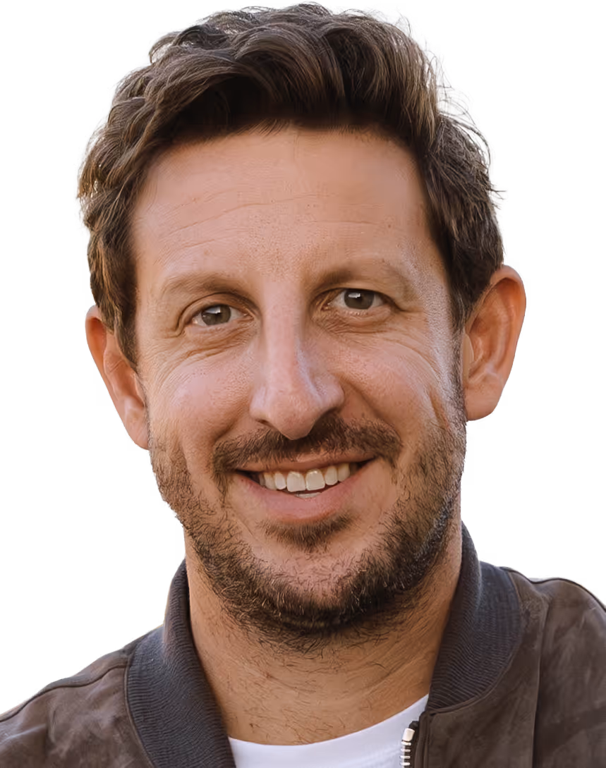 Smiling man with short brown hair, light beard, and brown eyes wearing a brown jacket and white shirt.