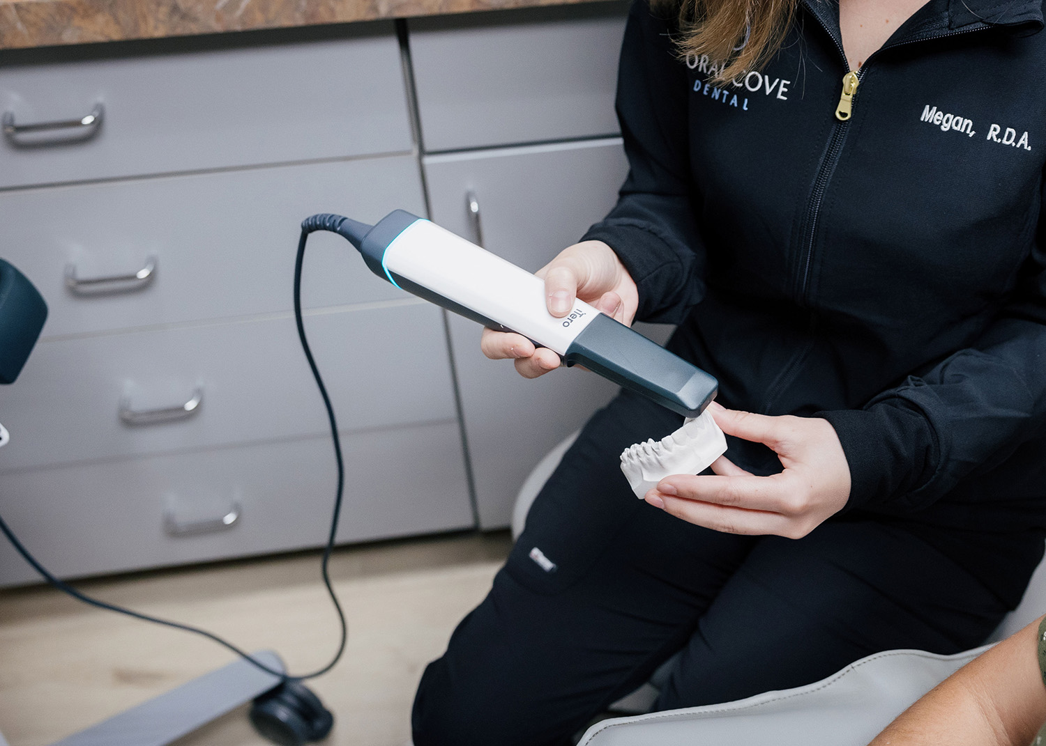 Dental professional holding a 3D intraoral scanner and a dental mold in a clinic setting.