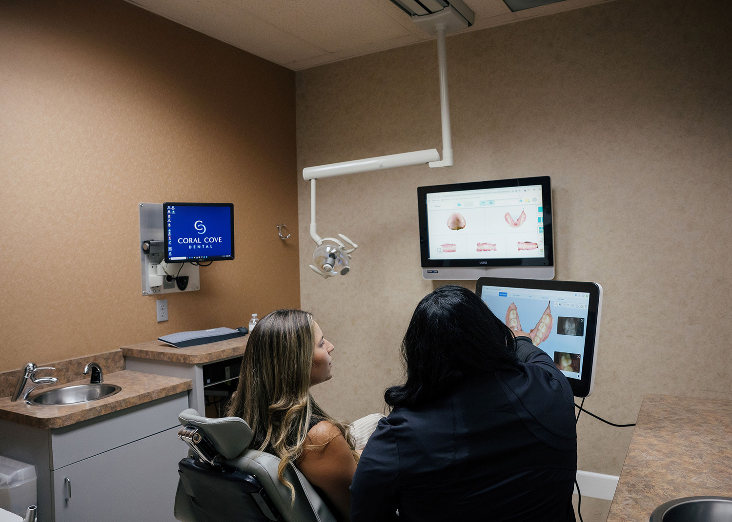 Dentist showing a female patient digital images of teeth on screens in a dental exam room.