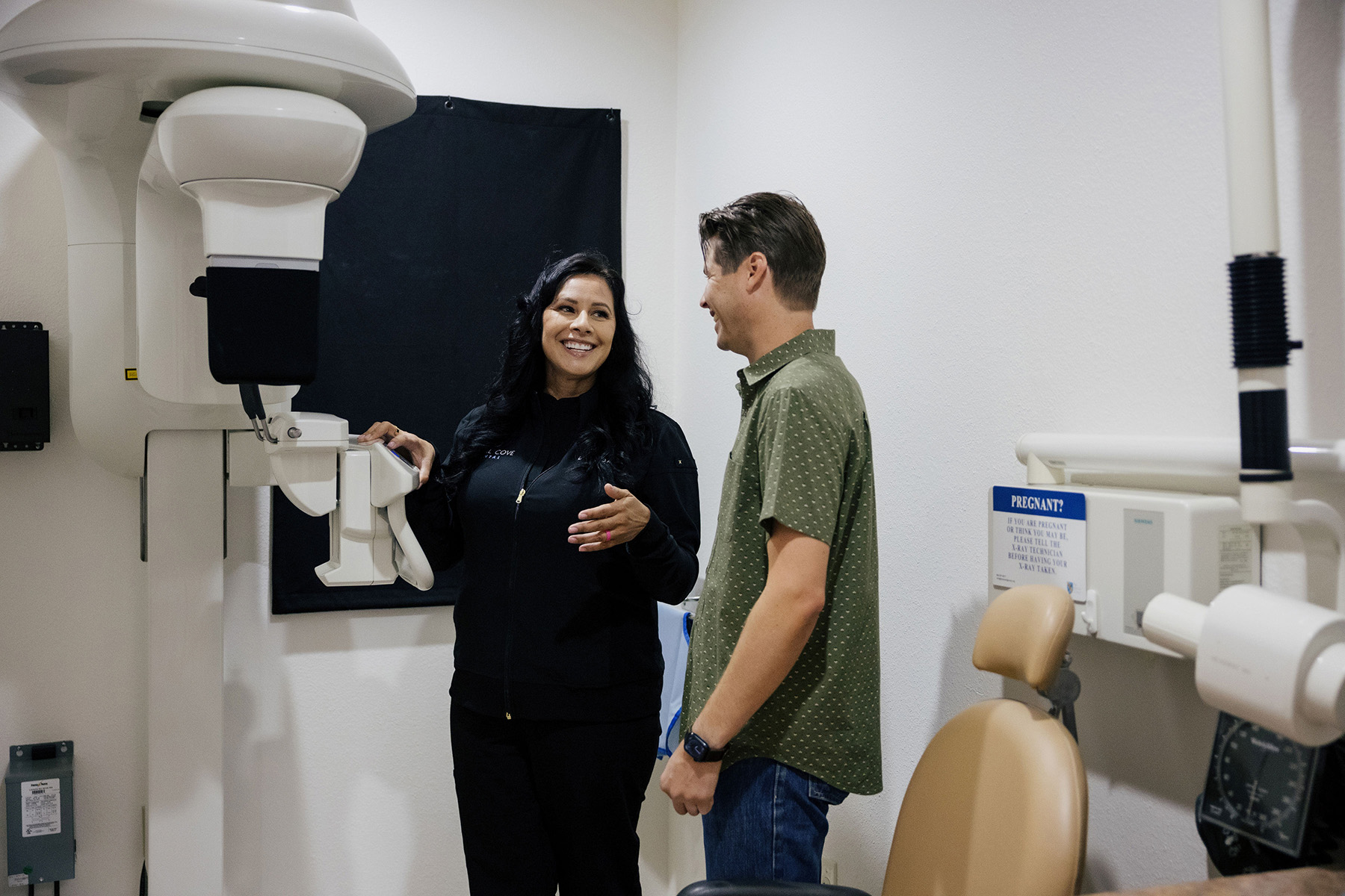 Female dental technician explaining X-ray machine to male patient in a dental clinic.