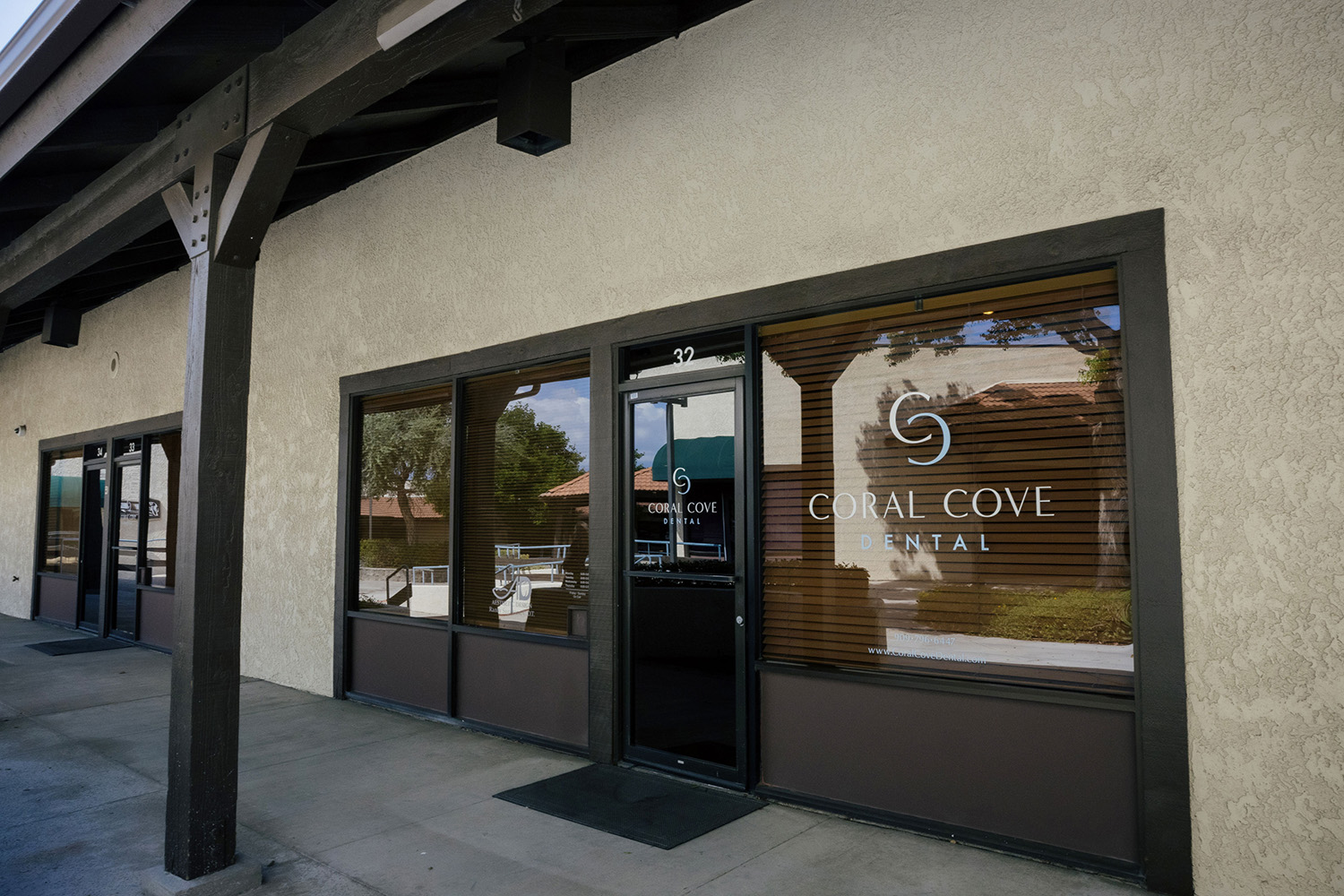 Exterior view of Coral Cove Dental office with large windows and entrance door under a covered walkway.