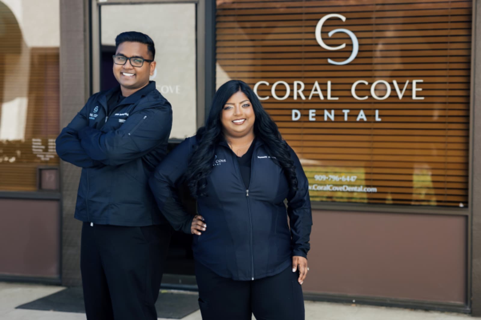 Male dentist and female staff member smiling in front of Coral Cove Dental sign