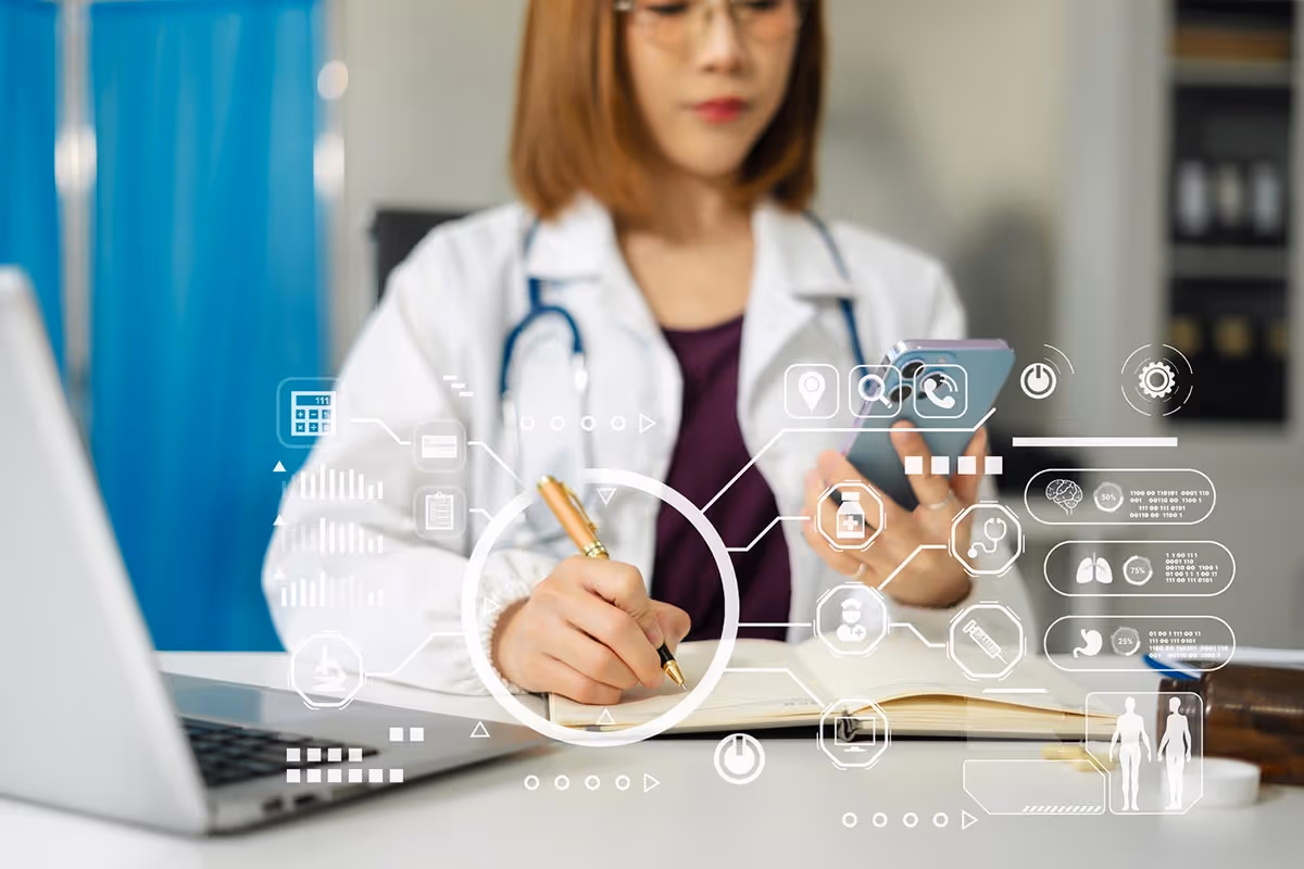 Female doctor using smartphone while writing notes at a desk with a laptop and medical icons overlay.