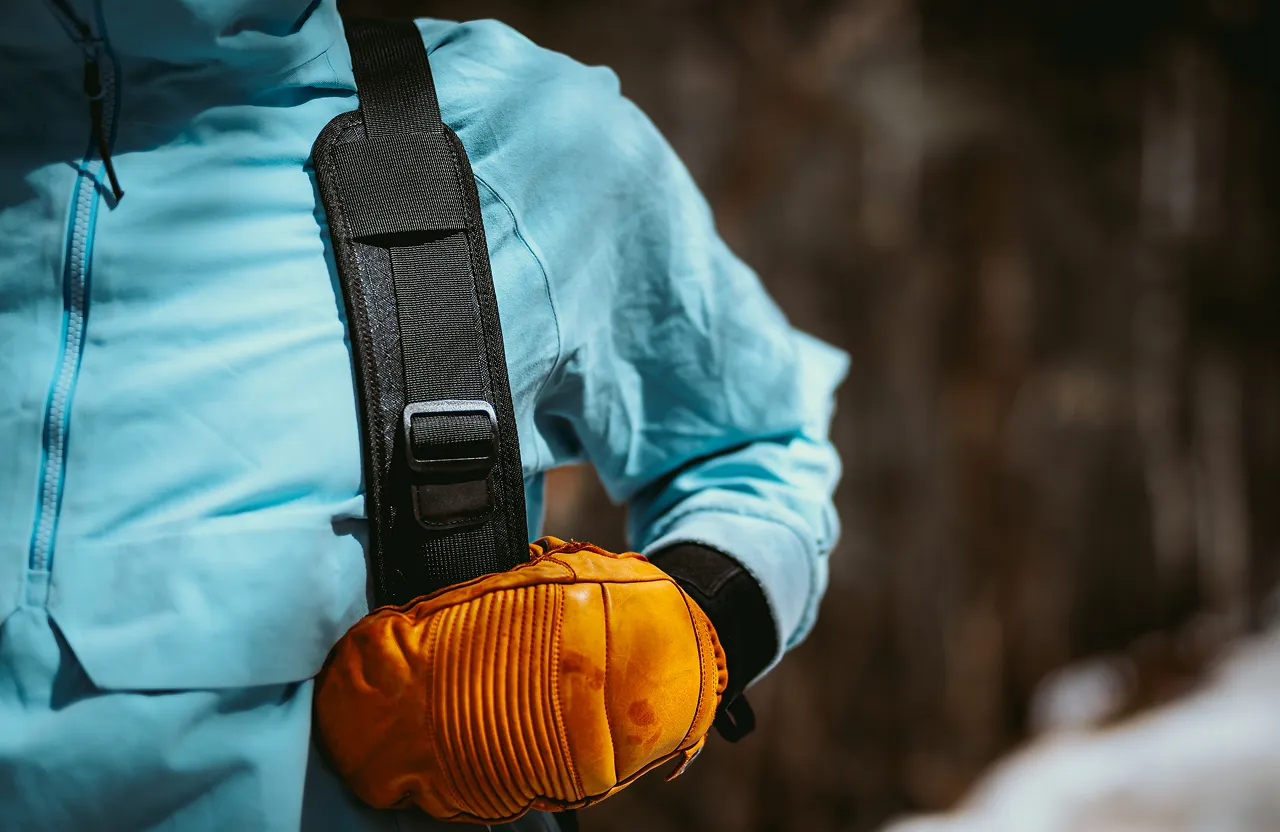 Person wearing a light blue jacket and holding an orange padded glove against a blurred brown background.