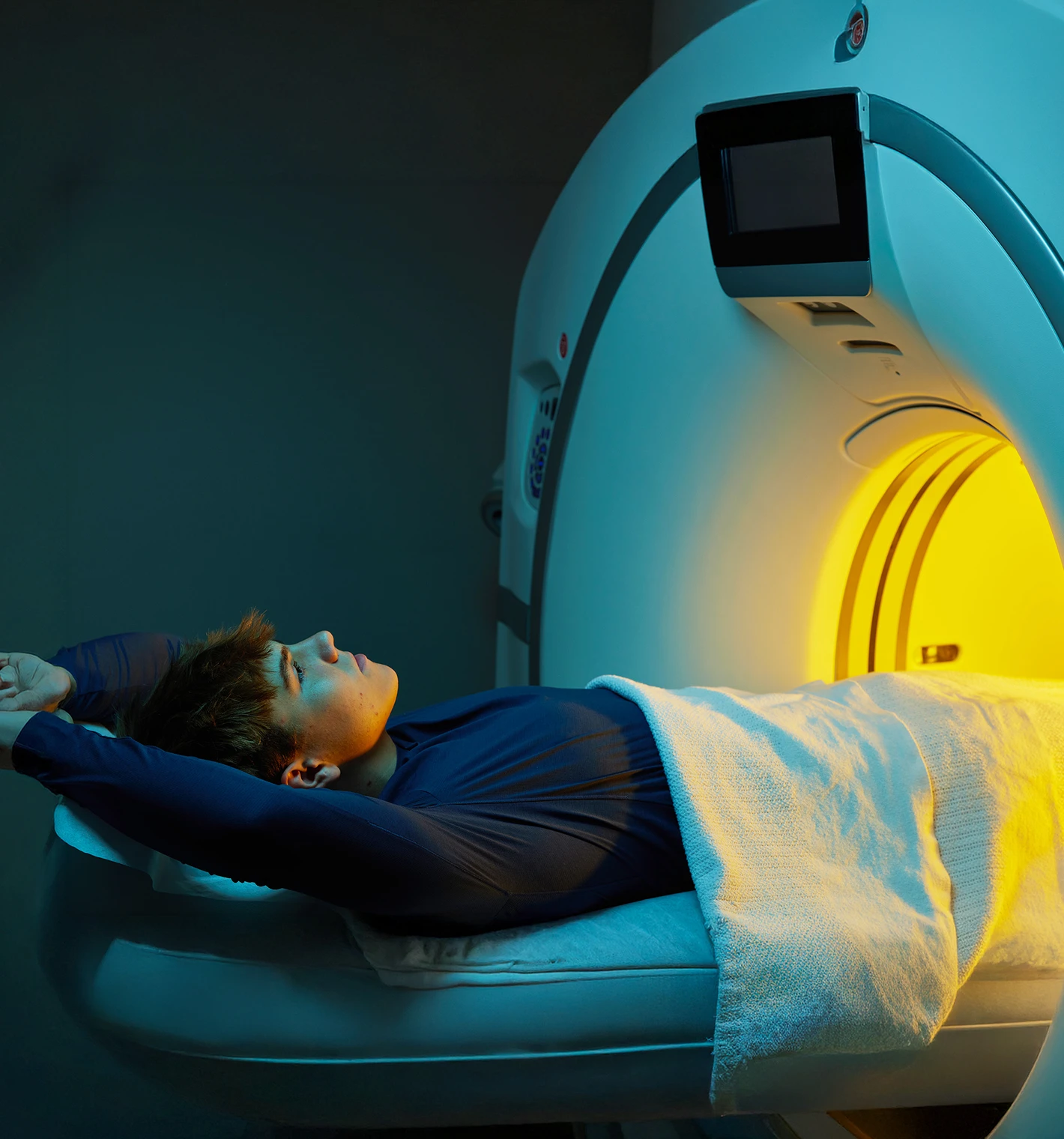 Person lying on a medical scanner bed, covered with a blanket, preparing for a scan inside a brightly lit MRI machine.