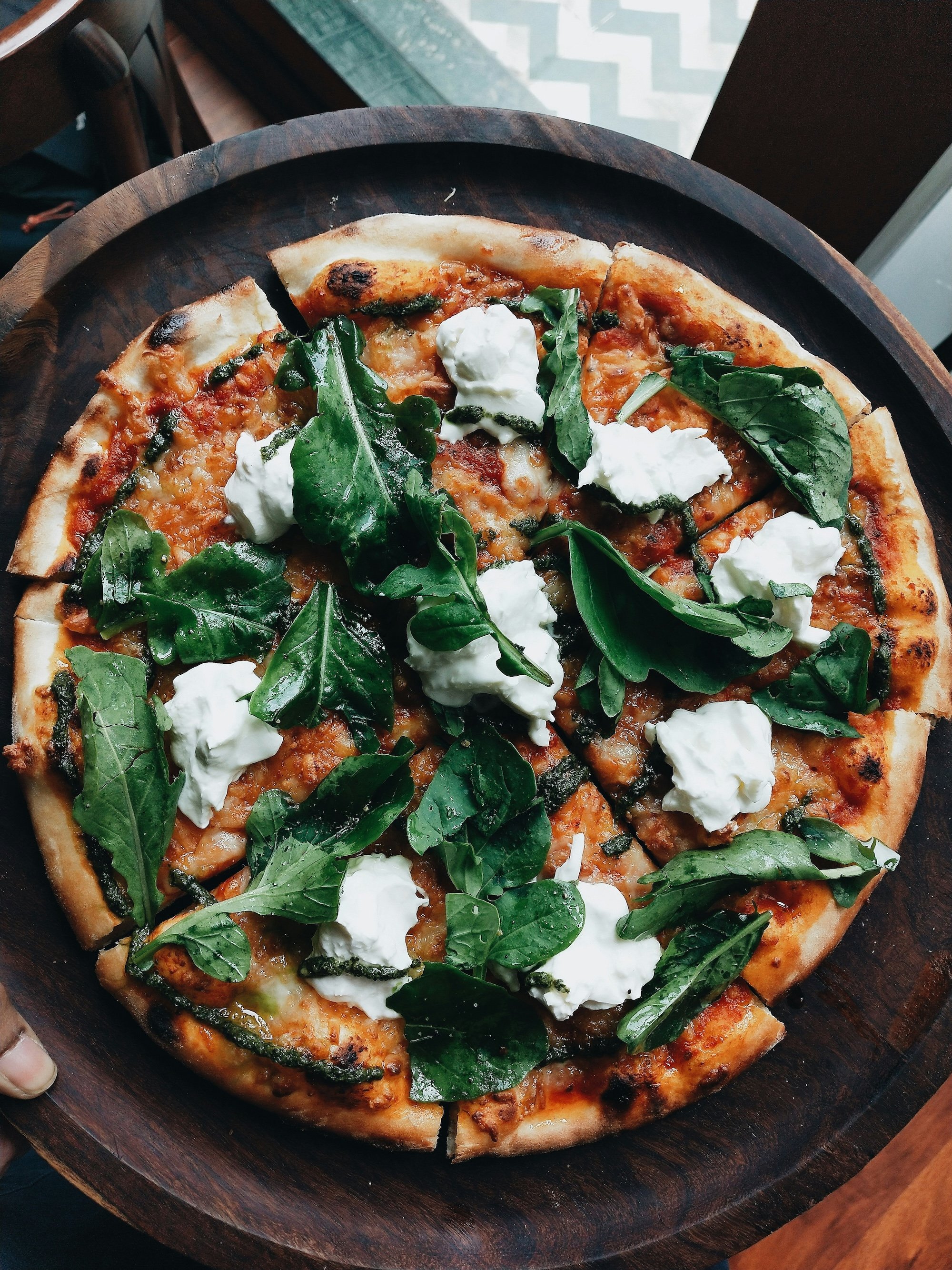 Pizza topped with fresh spinach leaves and dollops of ricotta cheese on a wooden serving tray.