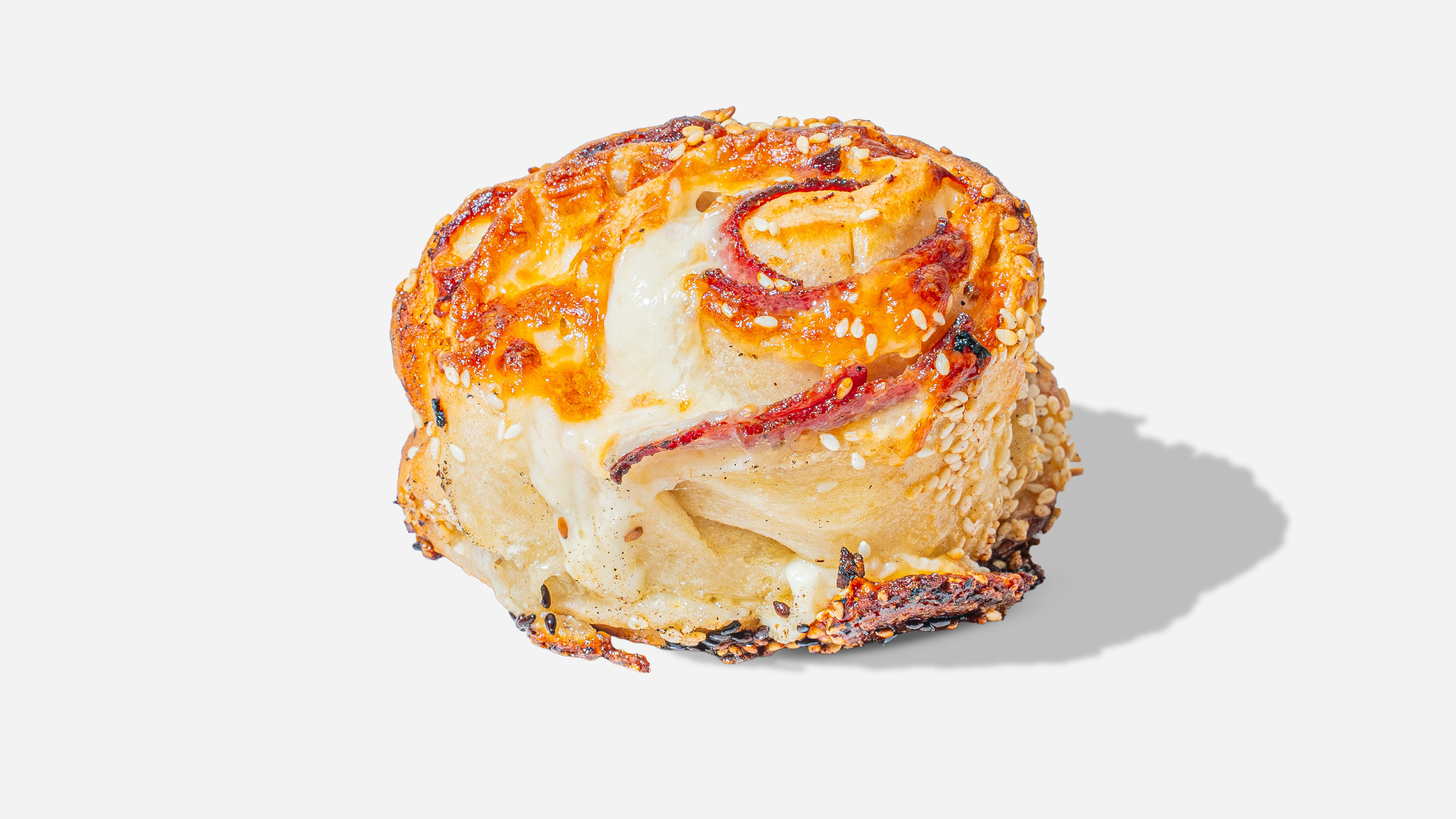 Close-up of a baked savory spiral roll with melted cheese, sesame seeds, and slices of pepperoni.