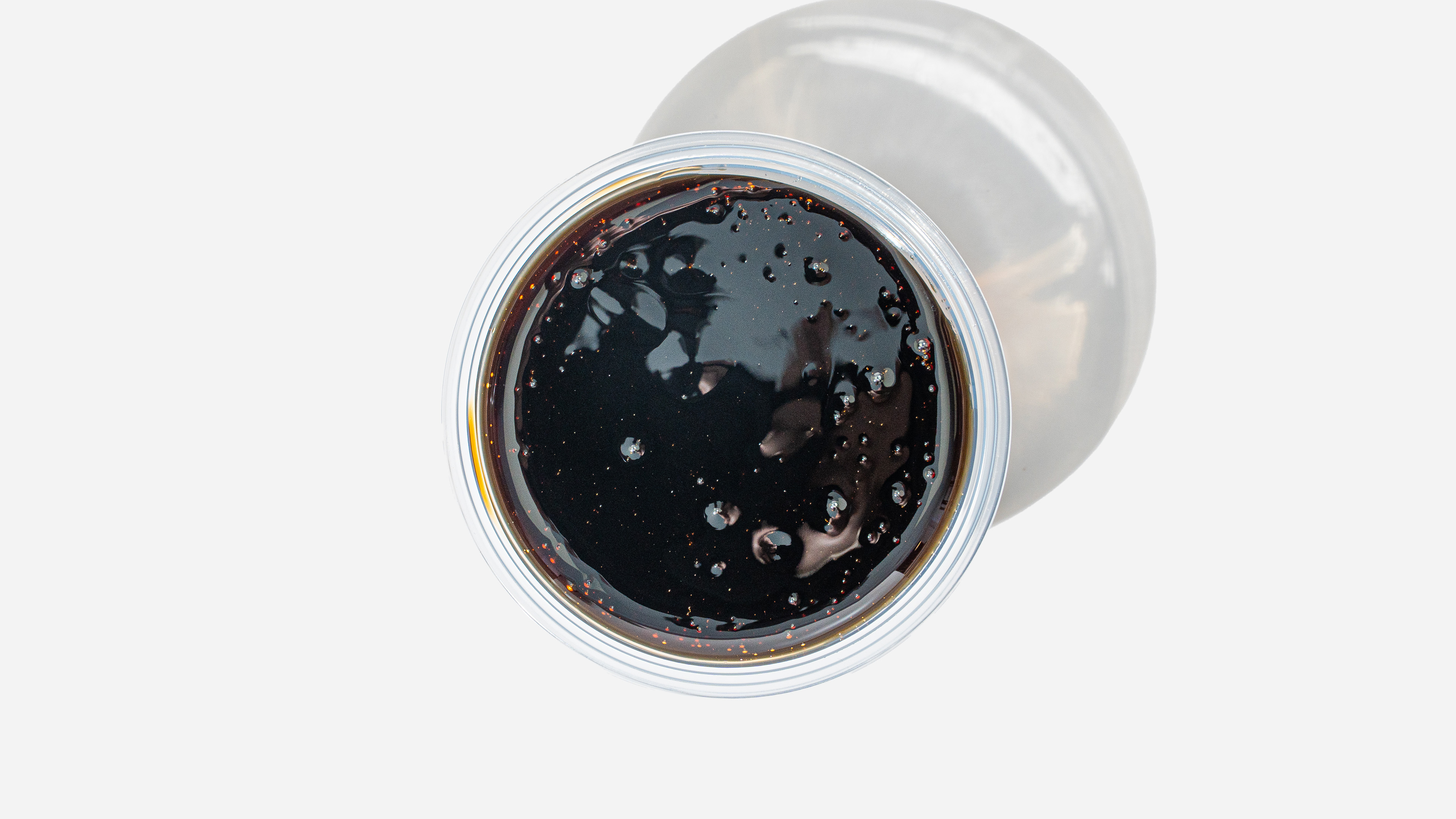 Top view of a cup filled with dark soda with bubbles on the surface and a faint shadow on a light background.