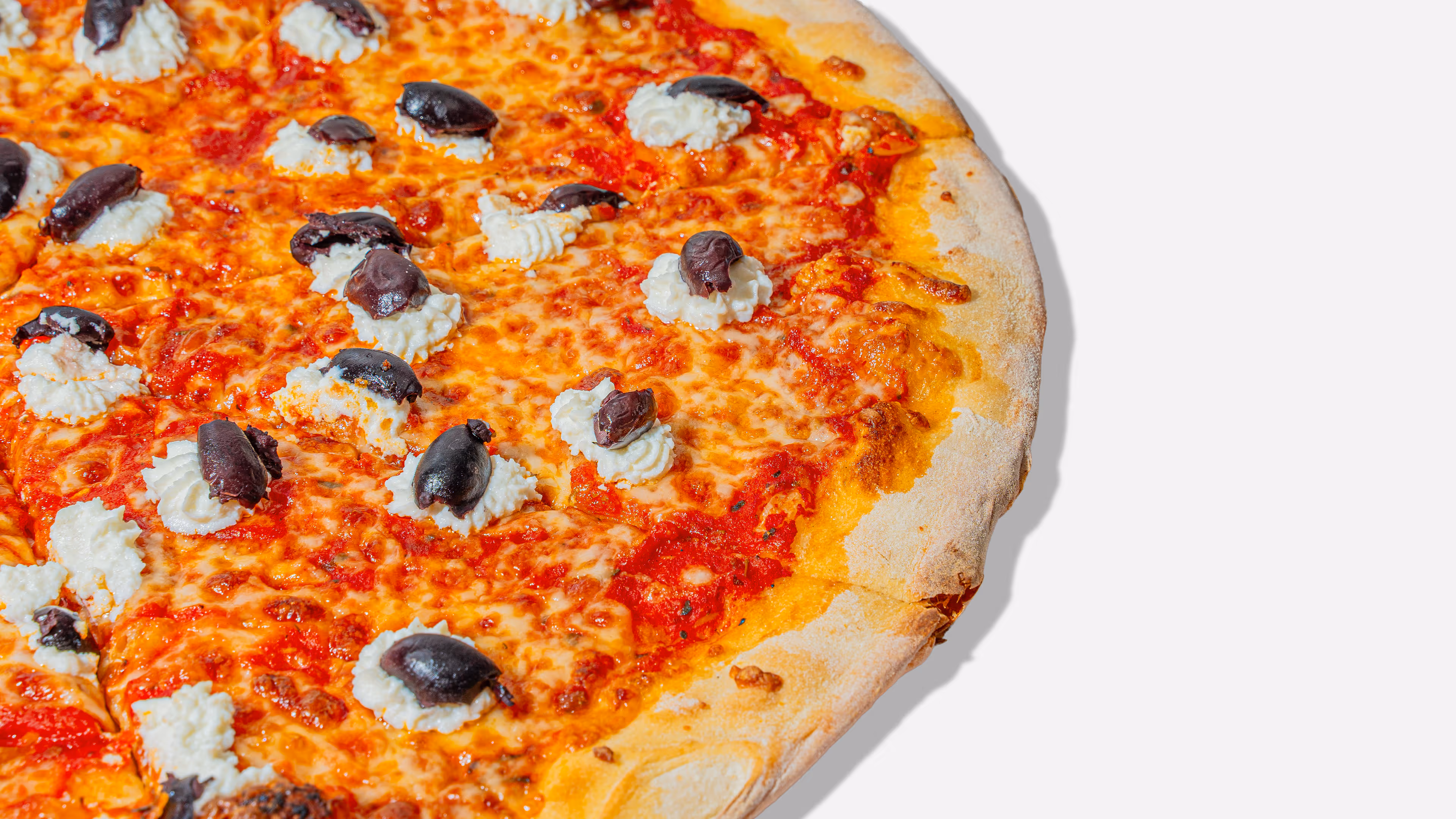 Close-up of a pizza with tomato sauce, melted cheese, dollops of ricotta cheese, and black olives on a golden crust.