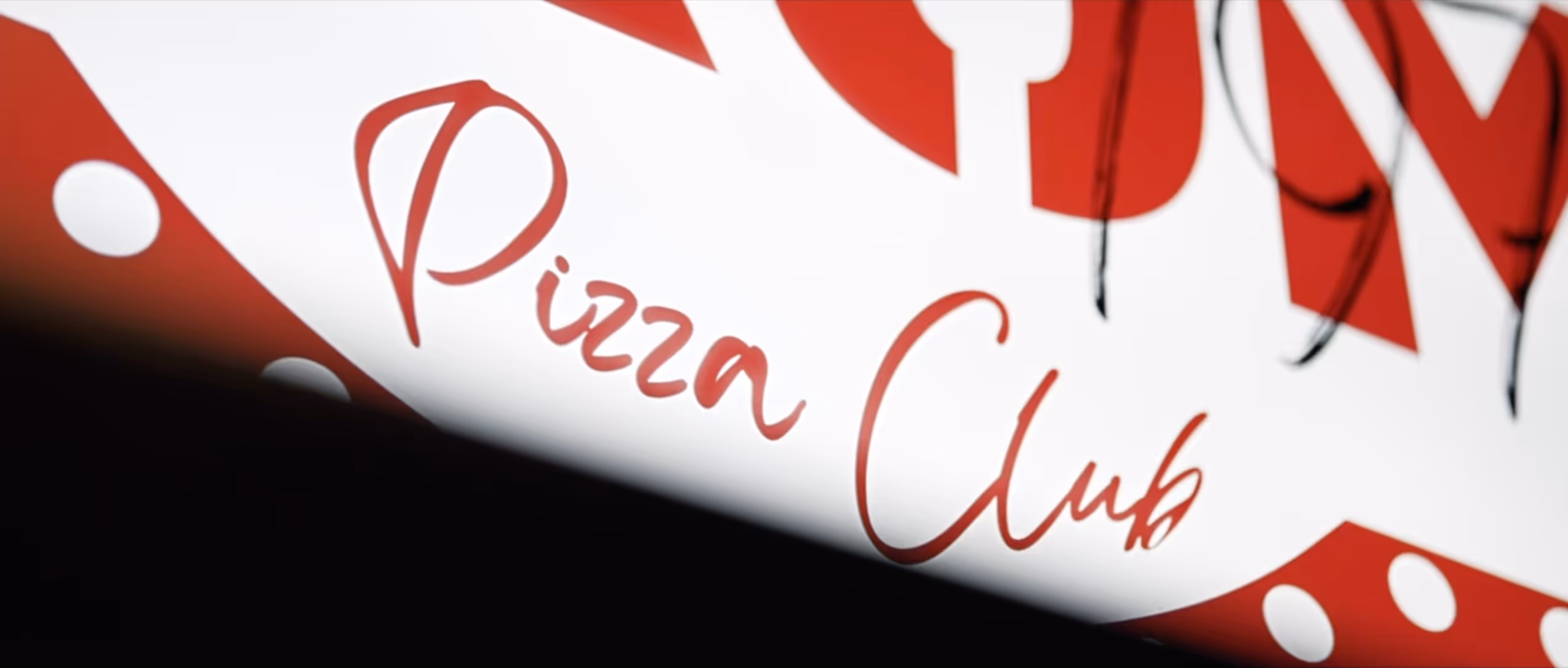 Close-up of a red and white sign with the words 'Pizza Club' in red cursive font.