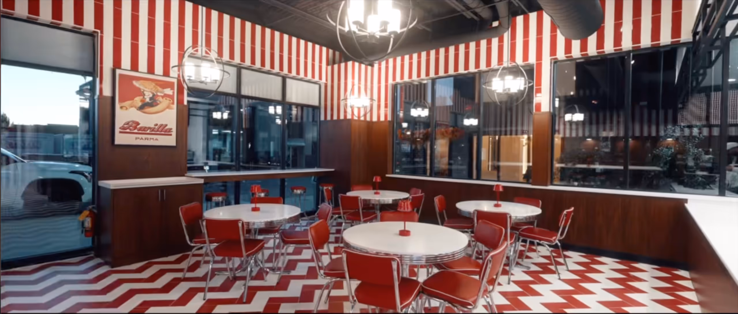 Retro diner with red and white chevron floor, red chairs, round white tables, and striped red and white walls.