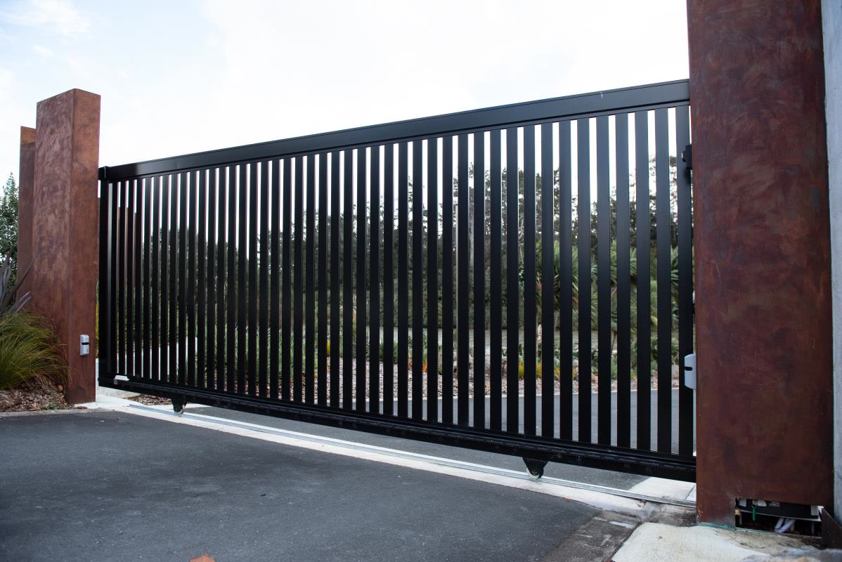 Black vertical slat driveway gate between rust-finished pillars