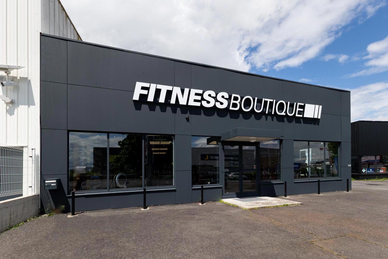 Façade d’un magasin Fitness Boutique avec une devanture noire et de grandes vitrines, situé dans une zone commerciale.