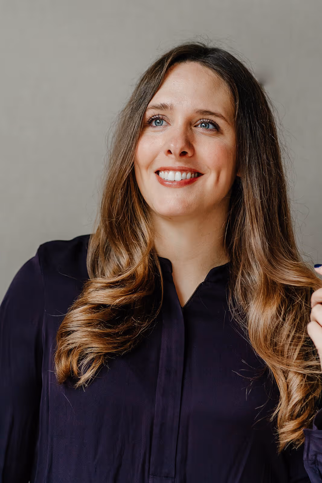 Smiling woman with long wavy hair wearing a dark blouse against a neutral background.