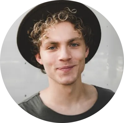 Usmívající se mladý muž s kudrnatými blond vlasy a černým kloboukem na světlém pozadí.