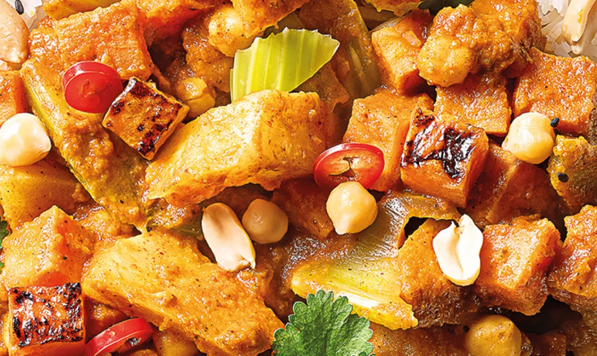 Detailní pohled na kořeněné pečené kousky tofu s pikantní omáčkou, arašídy, plátky chilli papričky a koriandrem.