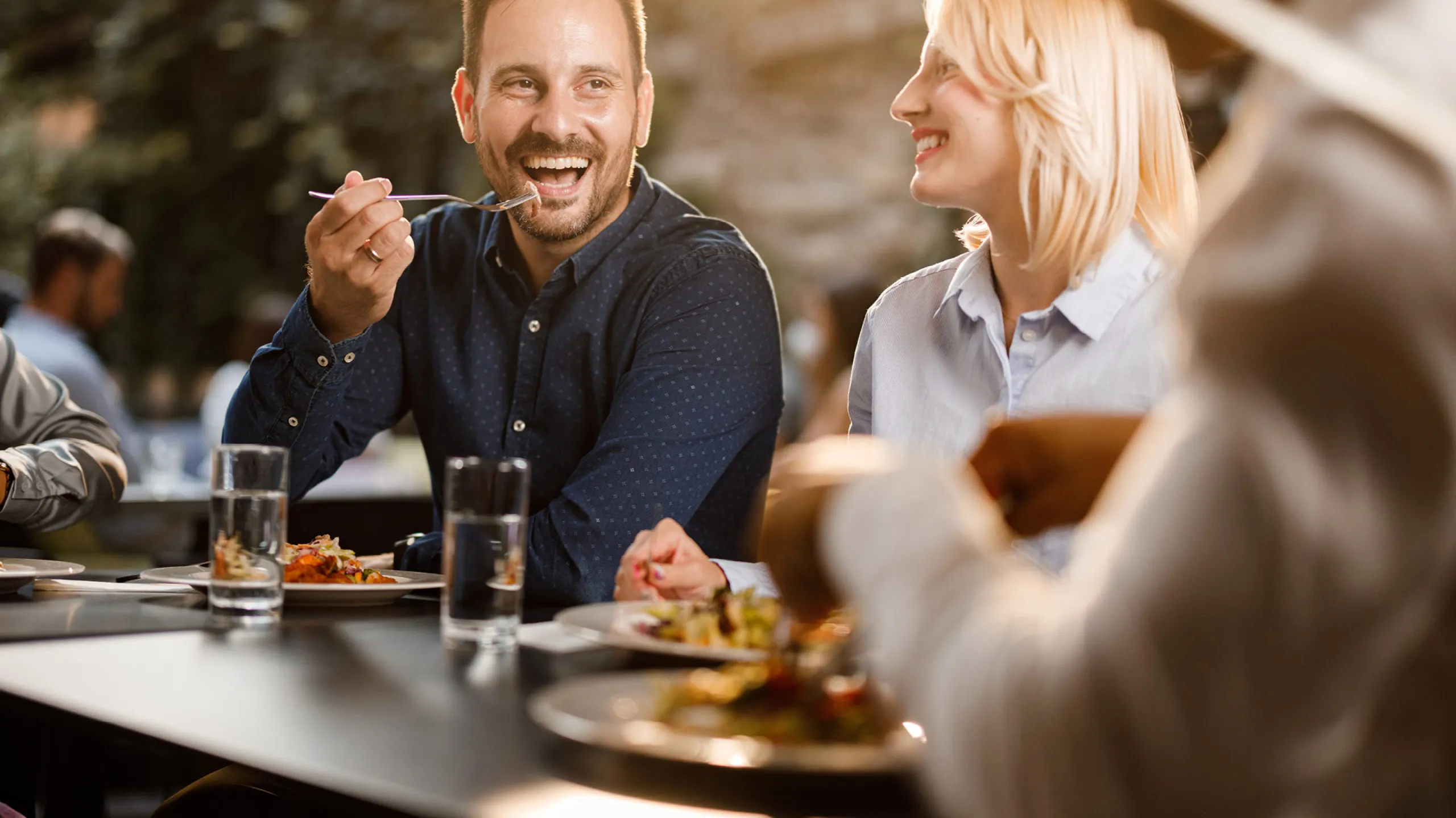 Dva lidé si užívají společný oběd a smějí se u stolu v restauraci.