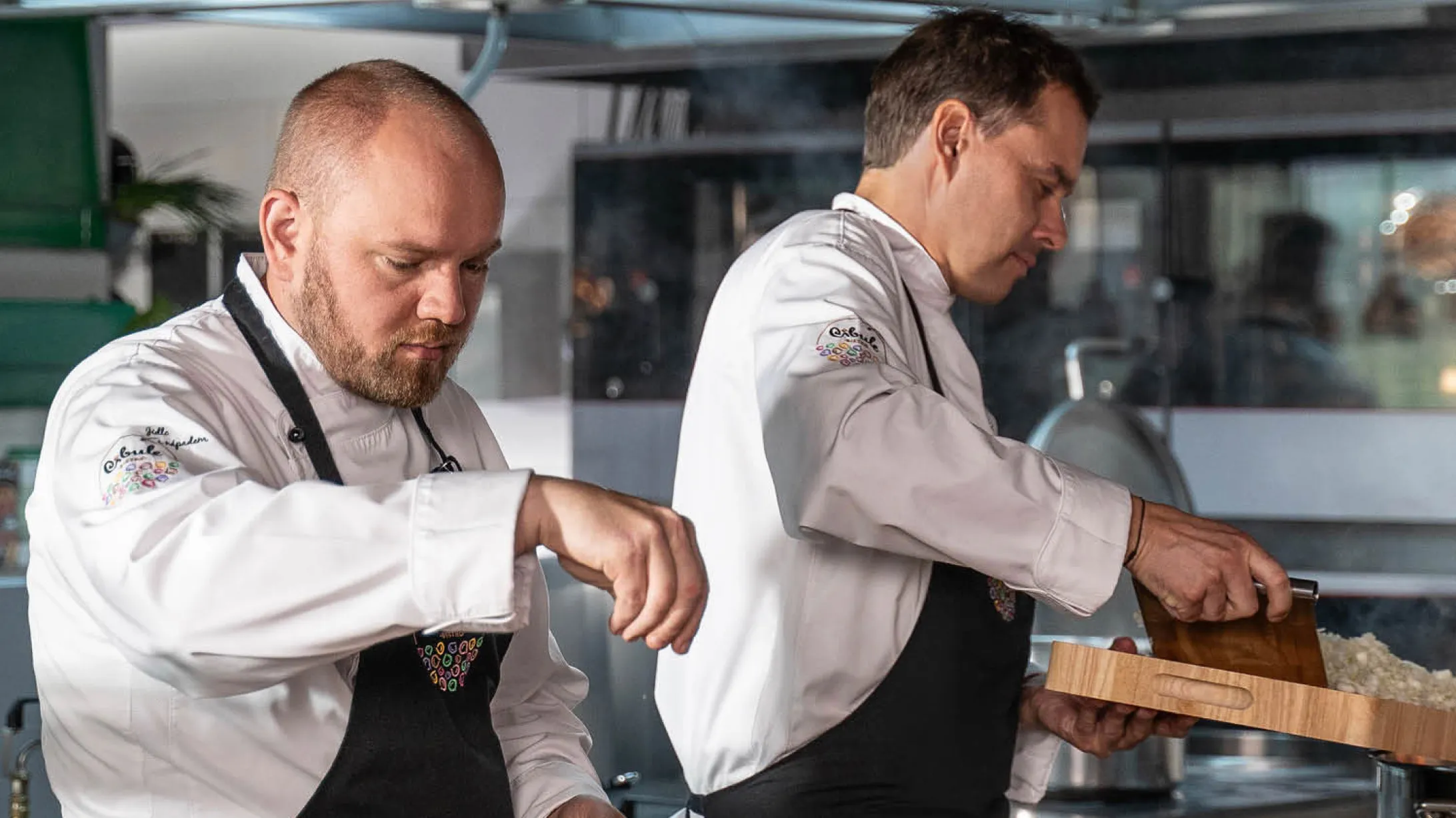 Dva muži v kuchařských uniformách připravují jídlo v profesionální kuchyni.