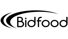 Štíhlá žena v zelených šatech se usmívá a sedí u žlutého stolu s bílými květinami a notebookem.