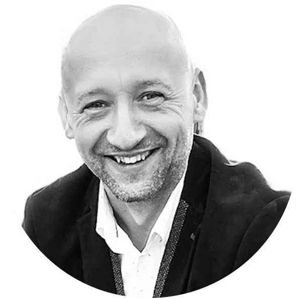 Muž s plešatou hlavou a vousy se usmívá a má na sobě sako s bílou košilí.