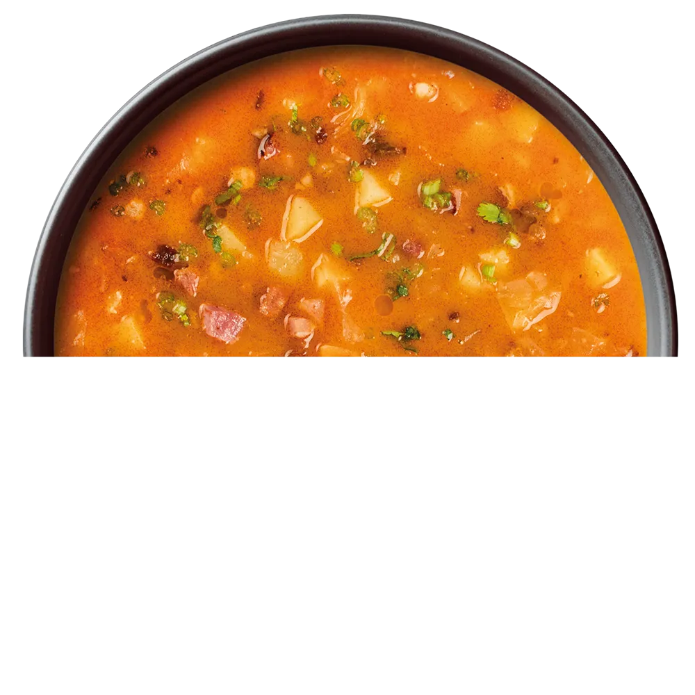 Miska polévky s červenou zelňačkou s kousky brambor, masa a zelených bylinek.